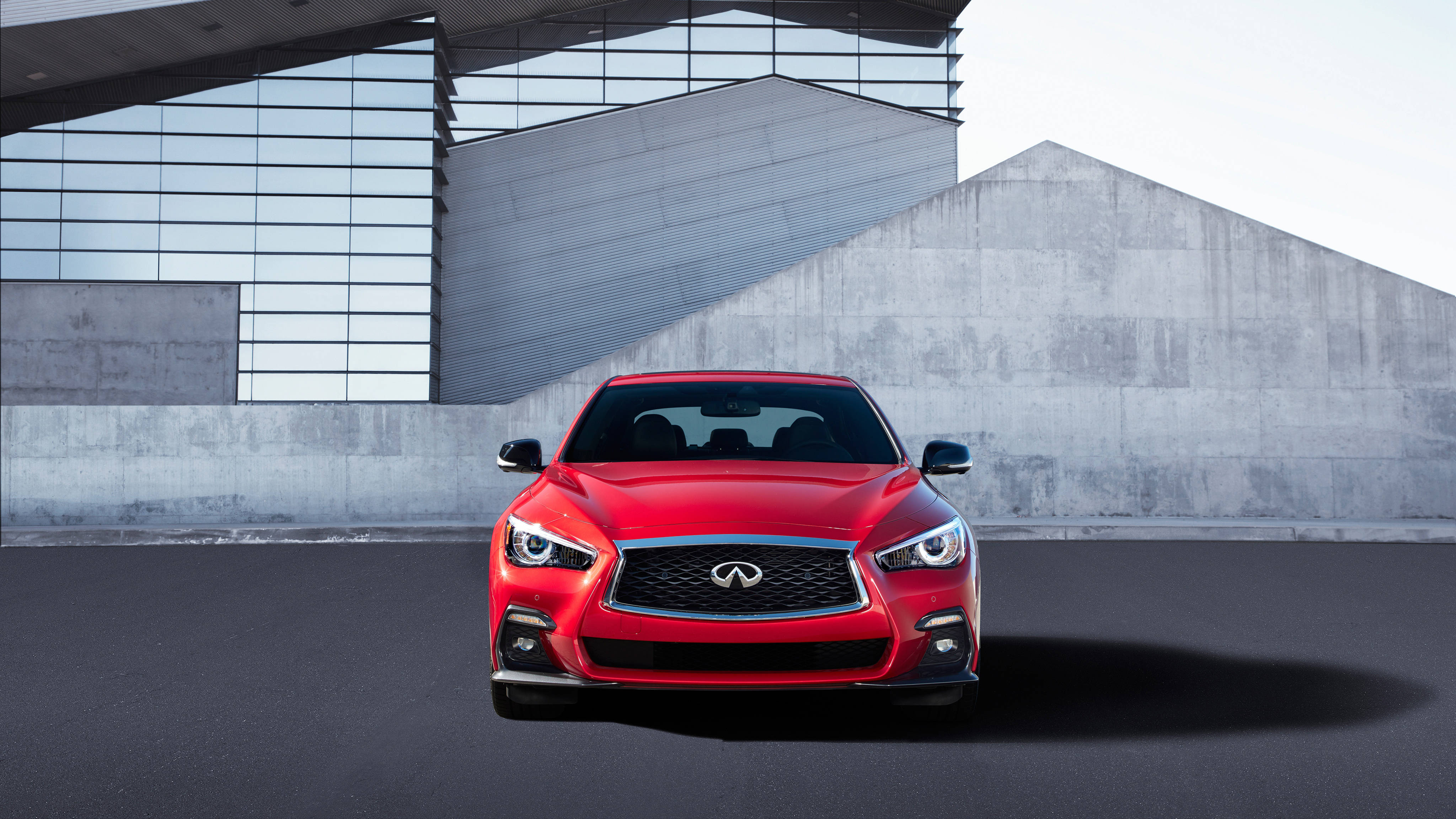 Infiniti 桌布 壁紙 — 一輛鮮紅色的Infiniti跑車正面朝向現代混凝土和玻璃建築背景。