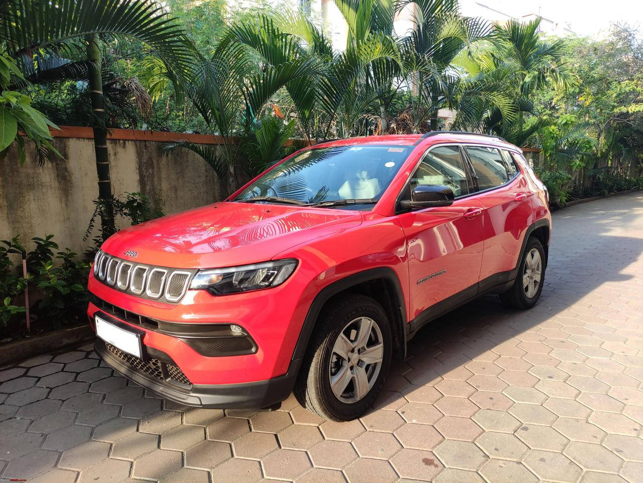 汽車 桌布 壁紙 — 一輛鮮紅色的Jeep Compass SUV停放在六角形瓷磚車道上，周圍環繞著茂密的熱帶植物。