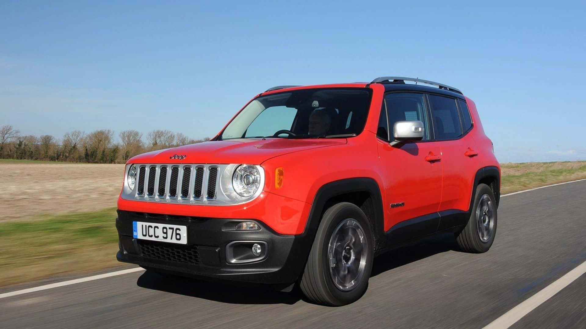 Jeep Renegade 桌布 壁紙 — 一輛鮮紅色的Jeep Renegade SUV在晴朗的藍天下，沿著陽光明媚的鄉村道路行駛，路邊是模糊的草地。