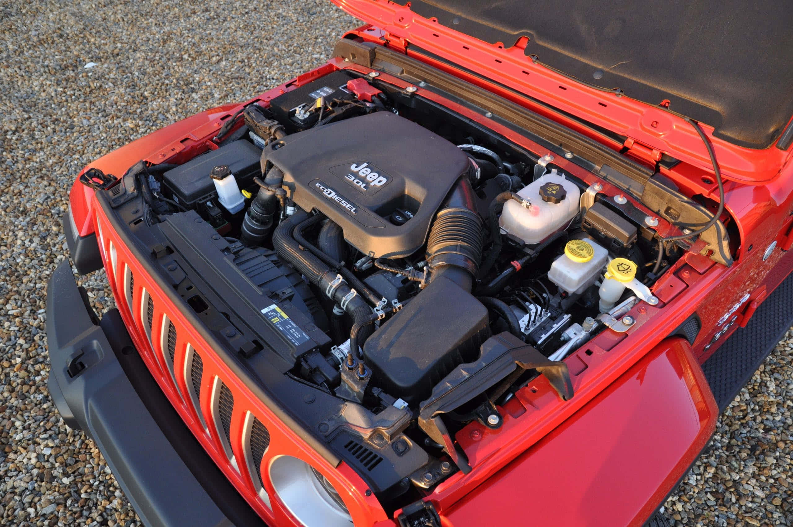引擎 桌布 壁紙 — 一輛鮮紅色的Jeep Wrangler打開引擎蓋，露出碎石地面上的詳細柴油引擎。