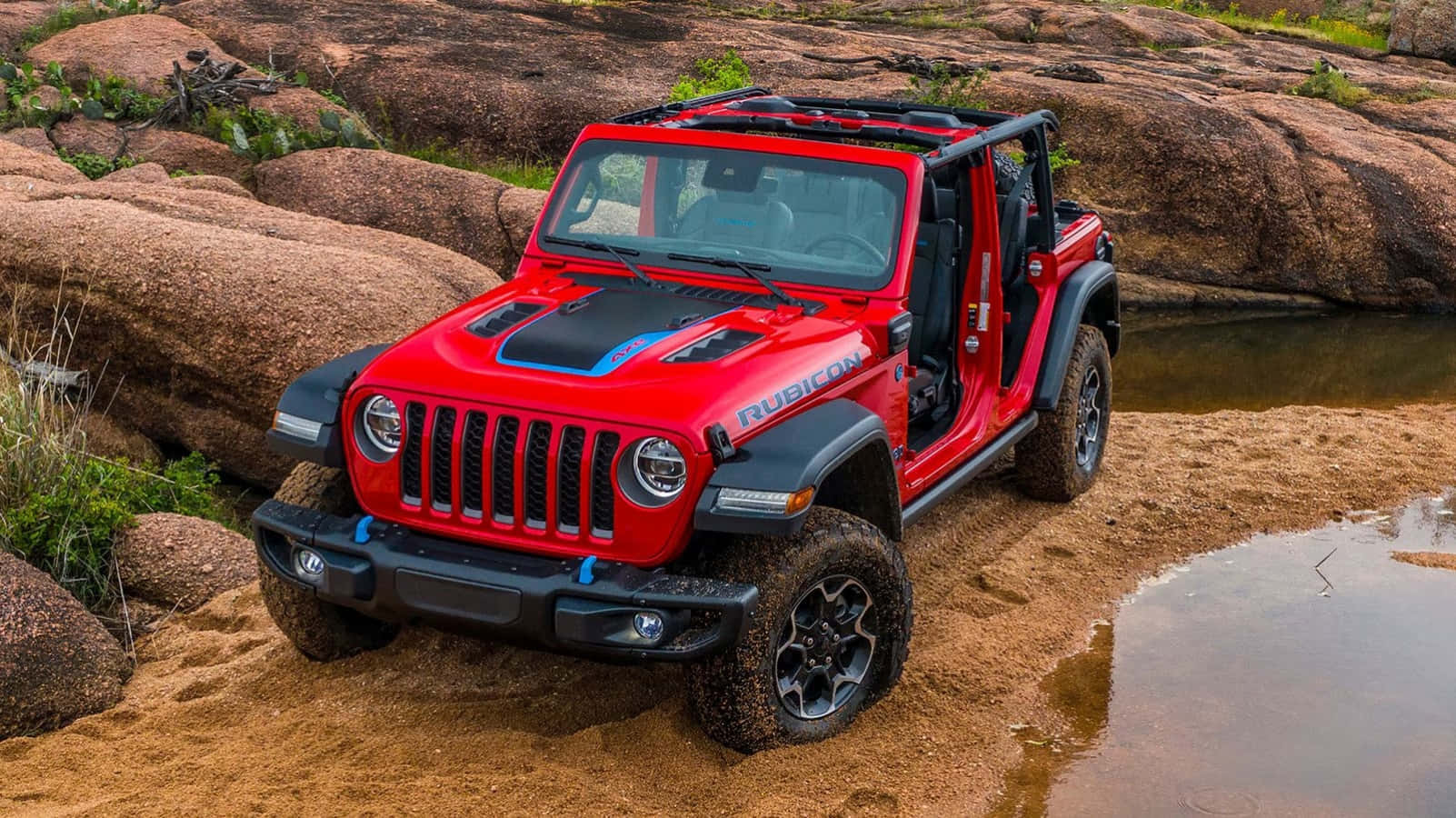 Jeep Wrangler 桌布 壁紙 — 一輛鮮紅色的Jeep Wrangler Rubicon在岩石沙漠溪流中堅固地站立，輪胎沾滿泥濘，車門敞開。