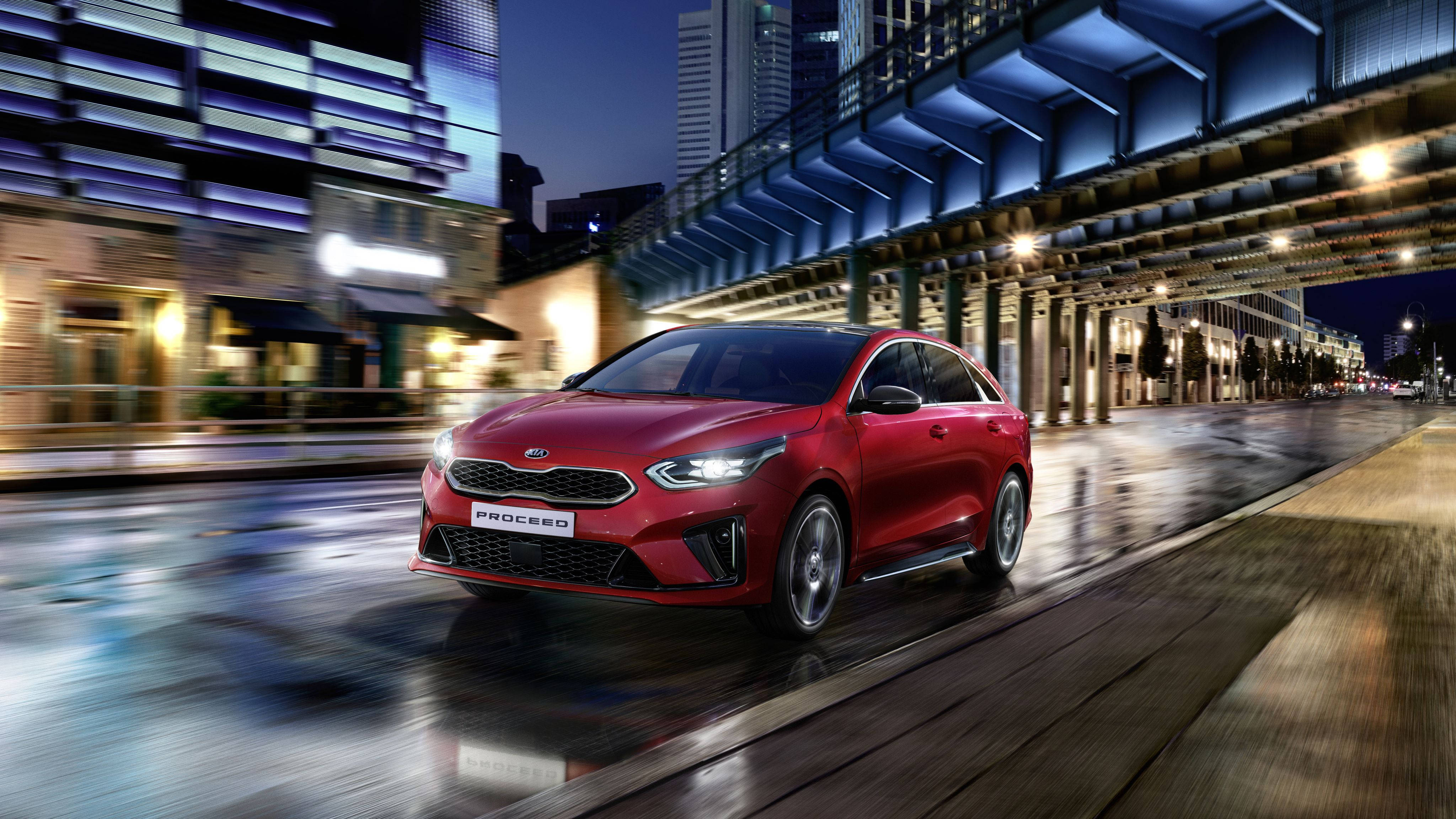 Kia 桌布 壁紙 — 一輛鮮紅色的Kia Proceed在夜間濕滑的城市街道上疾馳，帶有動態模糊效果，發光的城市燈光反射在路面上。
