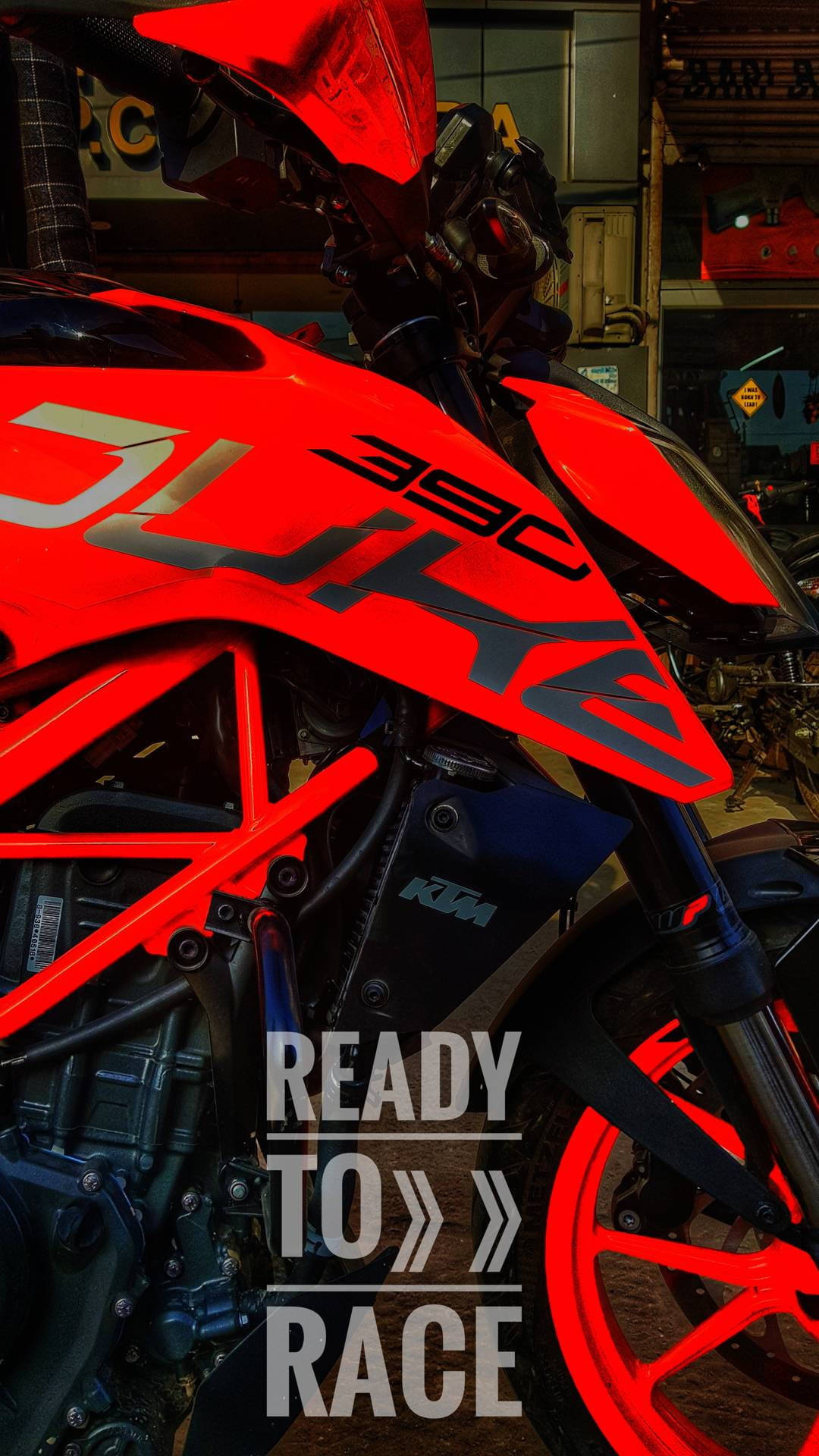 KTM 摩托車 桌布 壁紙 — 一輛鮮紅色的KTM Duke 390摩托車在車庫中戲劇性的燈光下閃閃發光，並以粗體文字宣告準備好比賽。