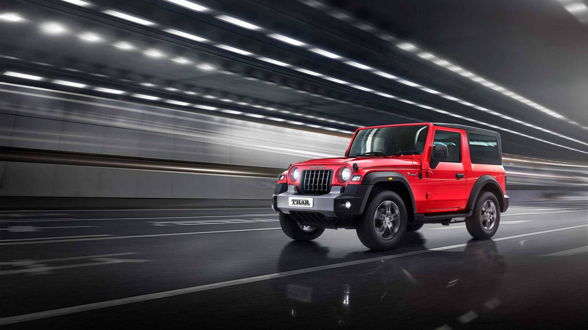 高清 桌布 壁紙 — 一輛鮮紅色的Mahindra Thar SUV在時尚的隧道中疾馳，頭頂上掠過動態模糊的燈光。