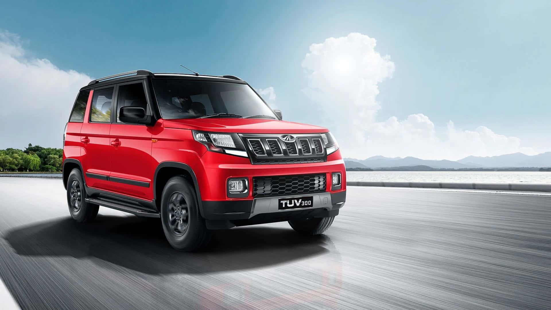 Mahindra 桌布 壁紙 — 一輛鮮紅色的Mahindra TUV300 SUV在明亮的藍天下沿著海岸道路疾馳，遠處有山巒。