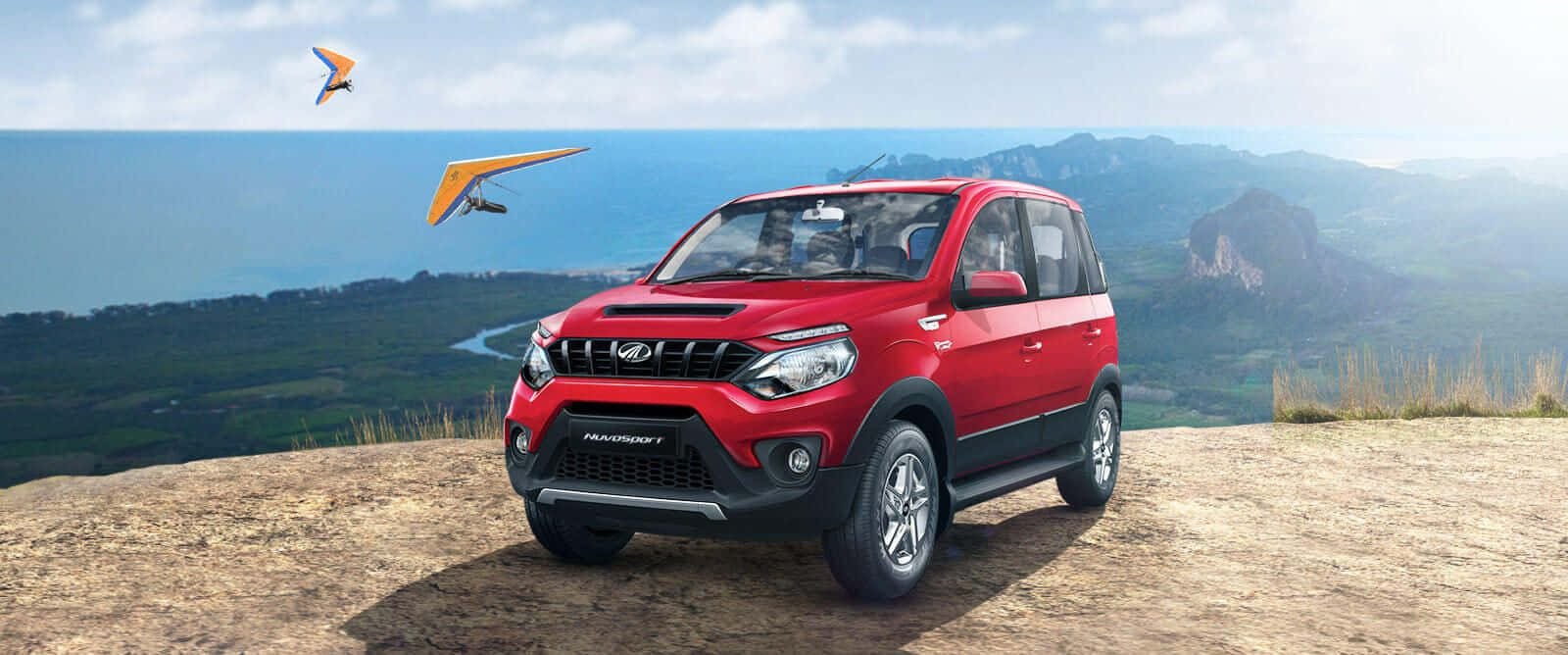Mahindra 桌布 壁紙 — 一輛鮮紅色的Mahindra TUV300 SUV停在懸崖上，俯瞰海岸山谷，有兩個滑翔傘在天空翱翔。