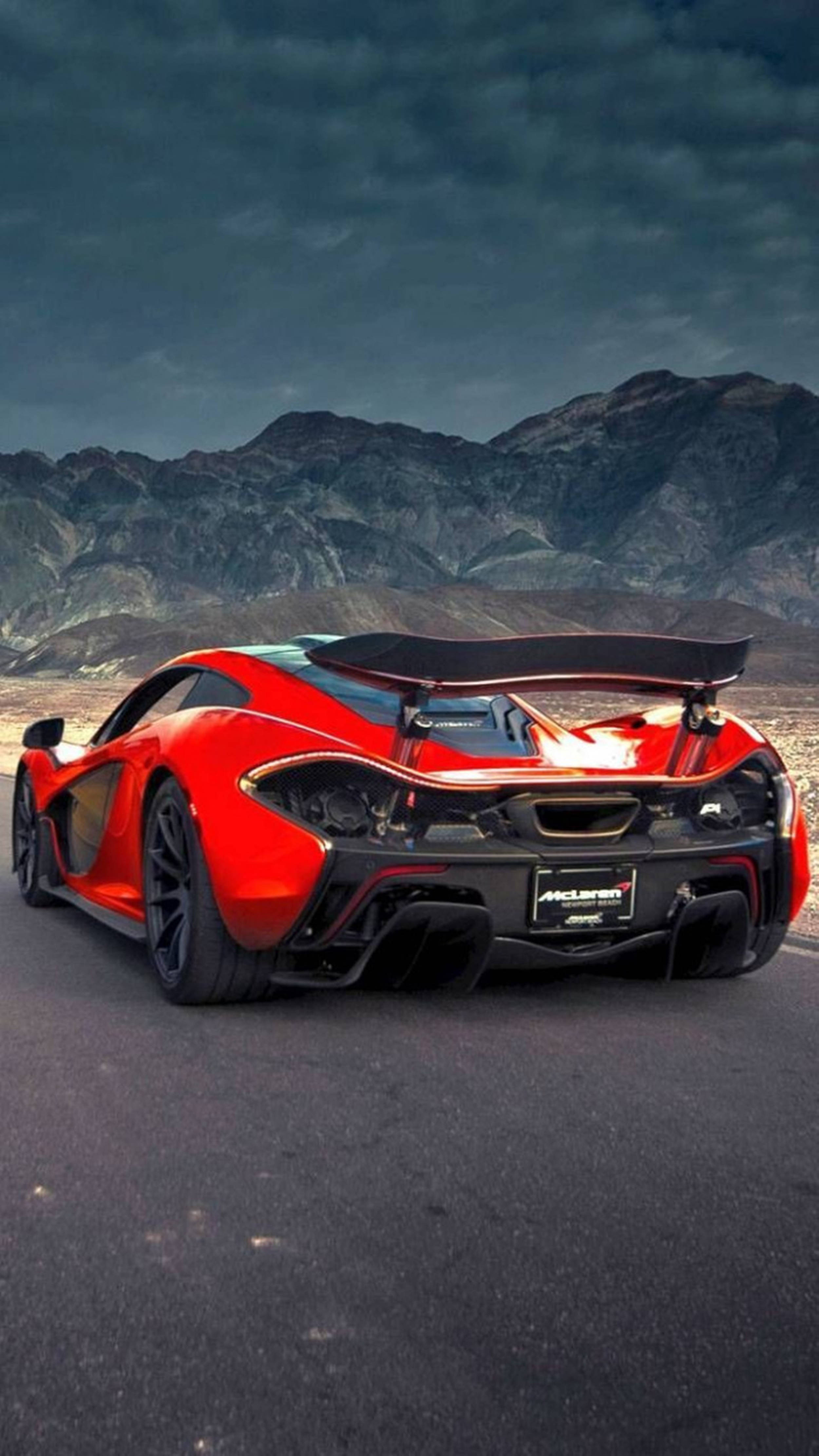 夜空 桌布 壁紙 — 一輛鮮紅色的McLaren跑車，帶有大型後擾流板，停在瀝青路上，背景是戲劇性的山脈和暴風雨的天空。