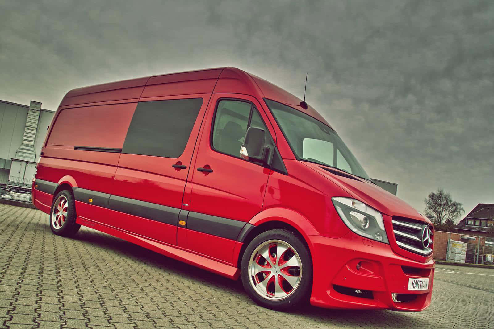Mercedes Benz Sprinter 桌布 壁紙 — 一輛鮮紅色的Mercedes-Benz Sprinter客貨車，配備定制合金輪圈，停放在鋪砌的停車場，天空多雲。