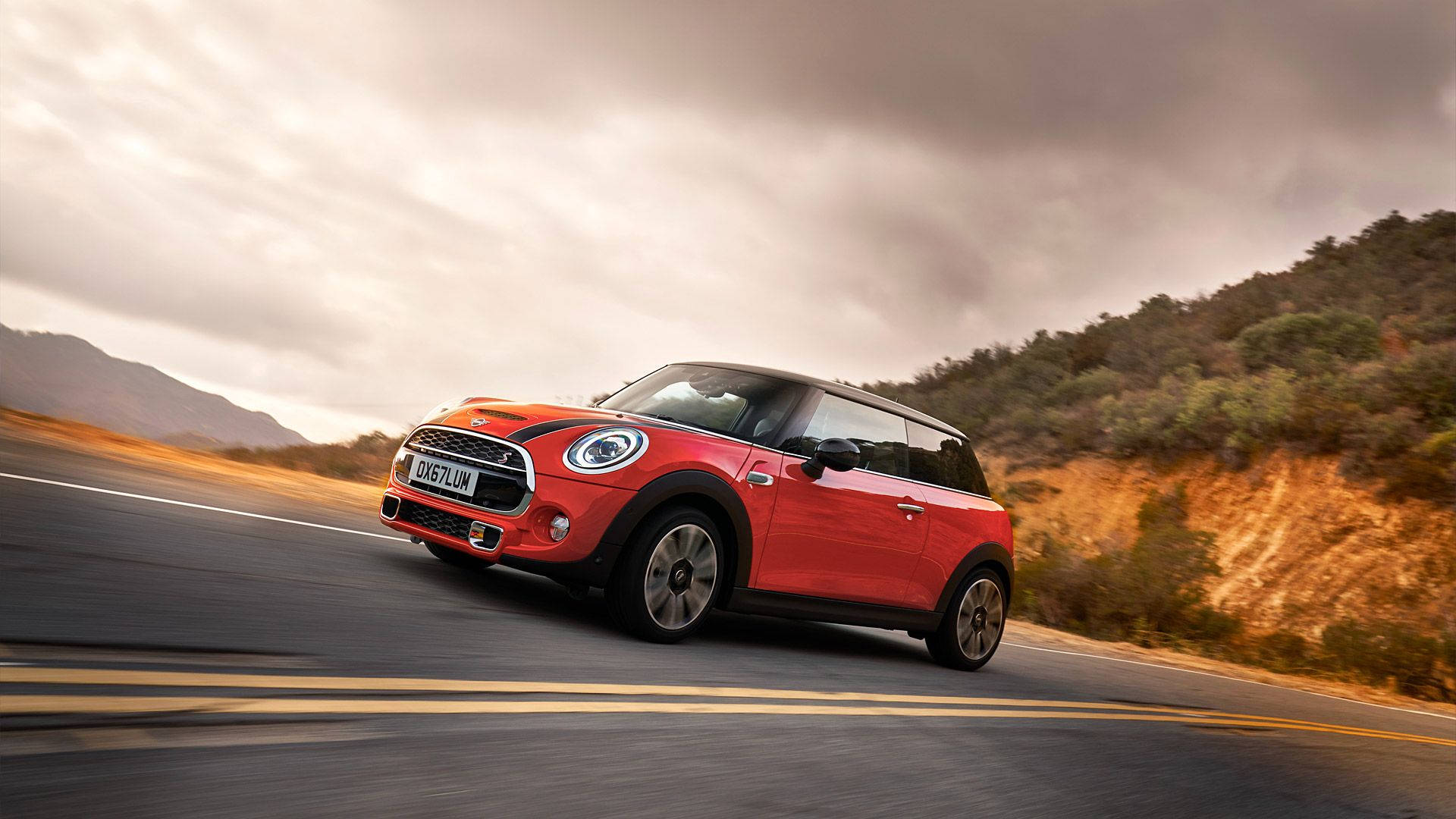 Mini Cooper 桌布 壁紙 — 一輛鮮紅色的Mini Cooper在陰沉多雲的天空下沿著蜿蜒的山路飛馳。