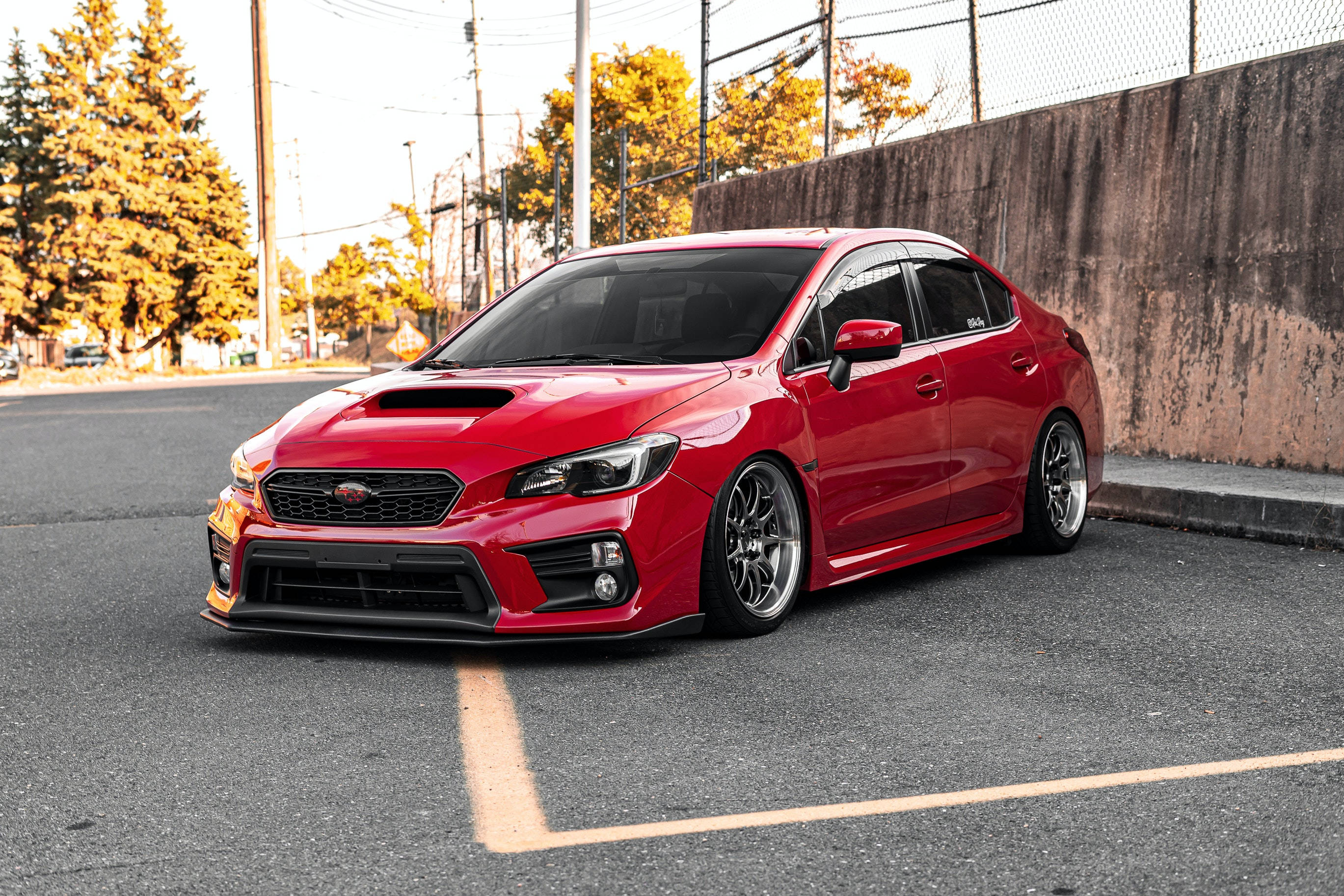 跑車 桌布 壁紙 — 一輛鮮紅色的Subaru WRX STI停在柏油路上，背景有秋天的樹木和一面混凝土牆。