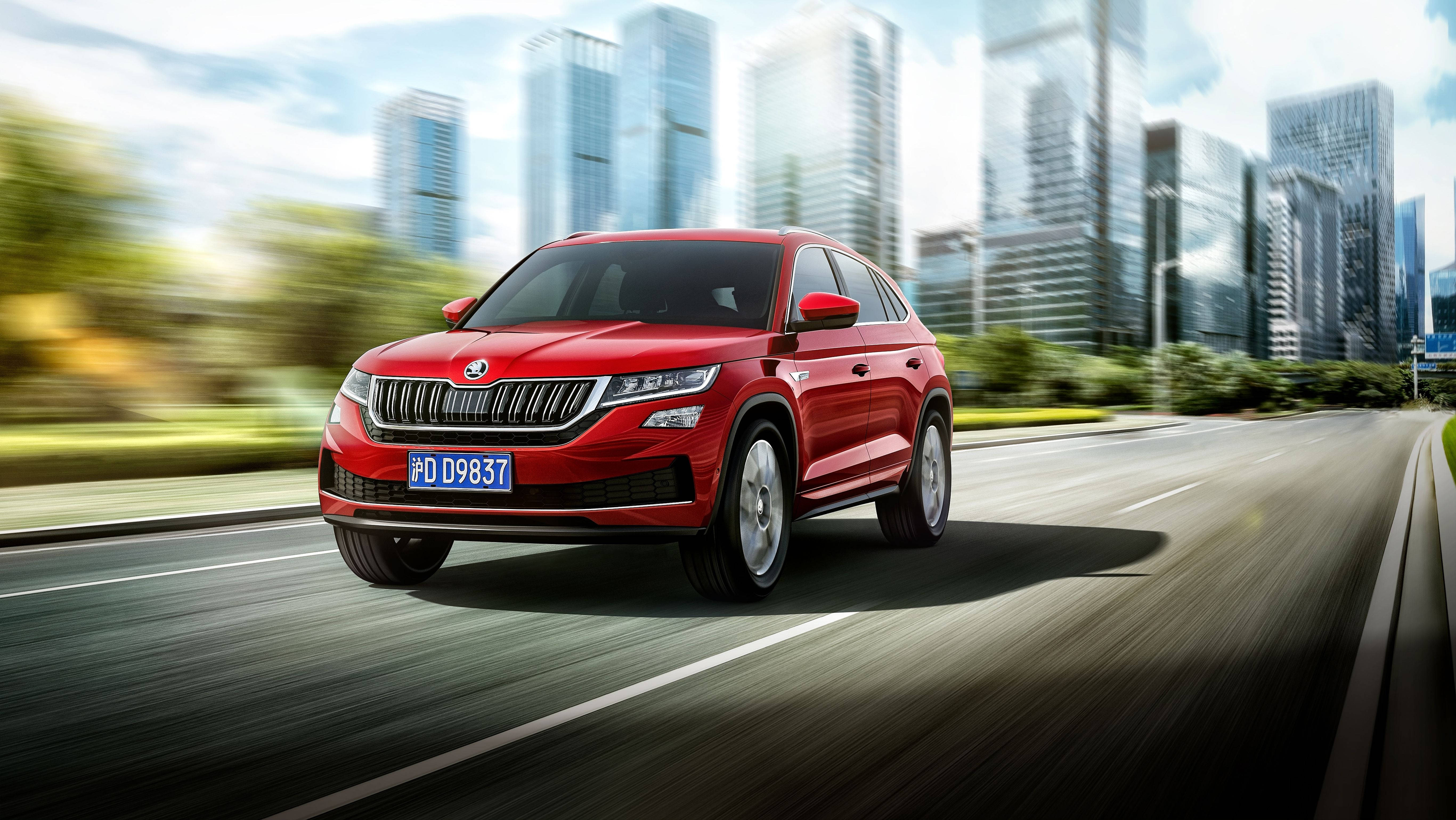 Skoda 桌布 壁紙 — 一輛鮮紅色的SUV在城市的公路上飛馳，模糊的摩天大樓和綠意在明亮的天空下掠過。