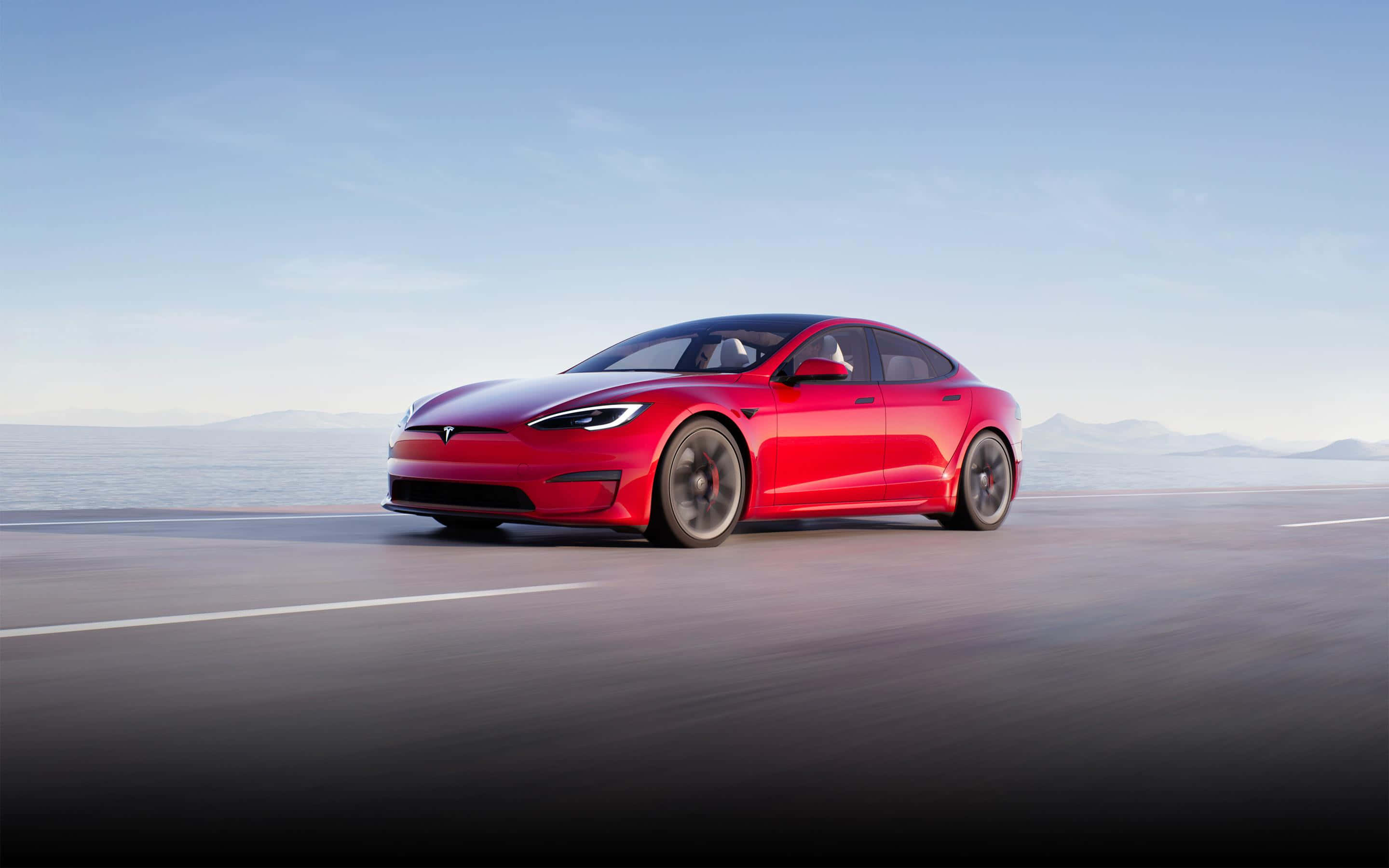 Red Car 桌布 壁紙 — 一輛鮮紅色的Tesla Model S在晴朗藍天下沿著海岸公路行駛，遠處有山巒。
