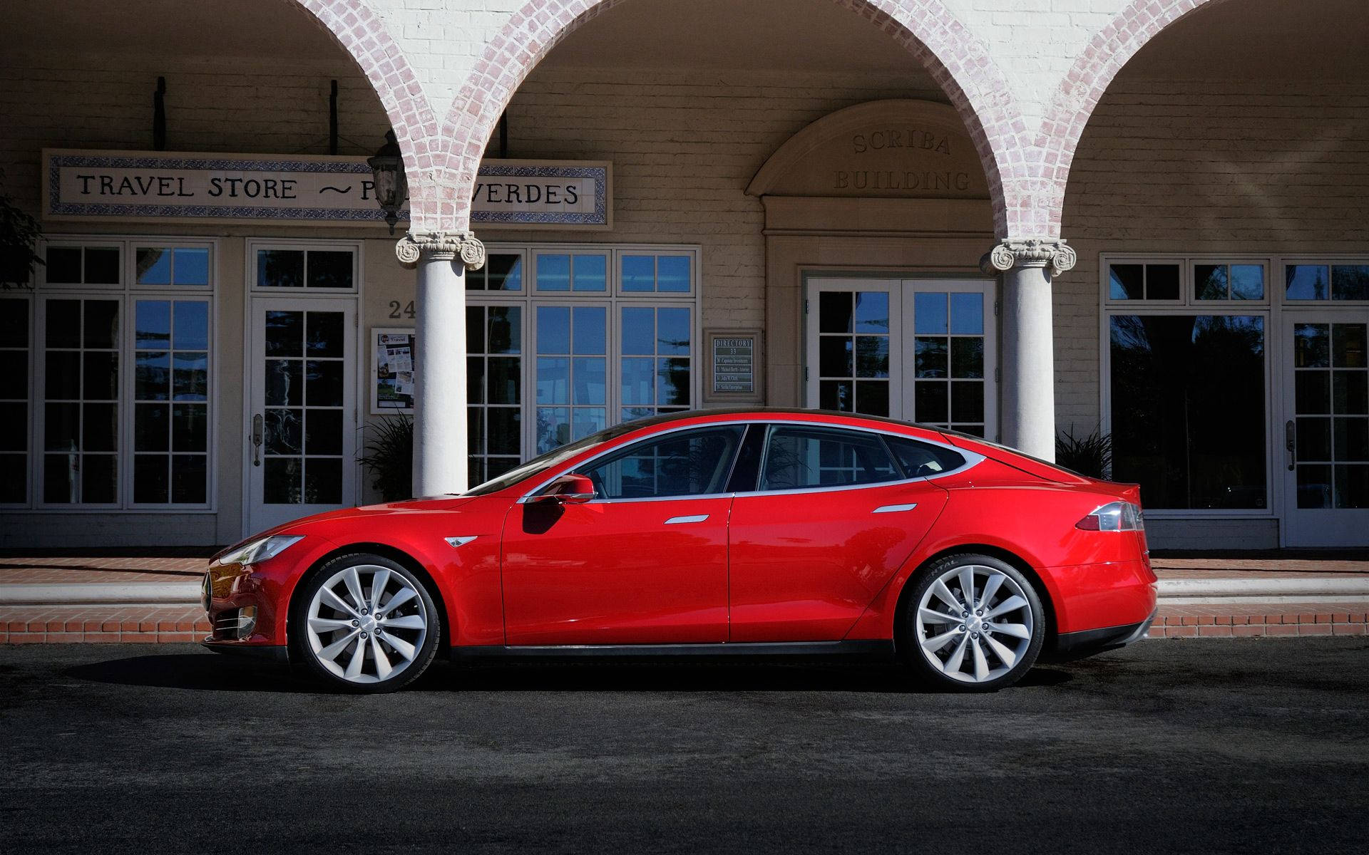 特斯拉 桌布 壁紙 — 一輛鮮紅色的Tesla Model S轎車停放在歷史悠久的磚砌建築的拱形門廊下，該建築設有玻璃門。