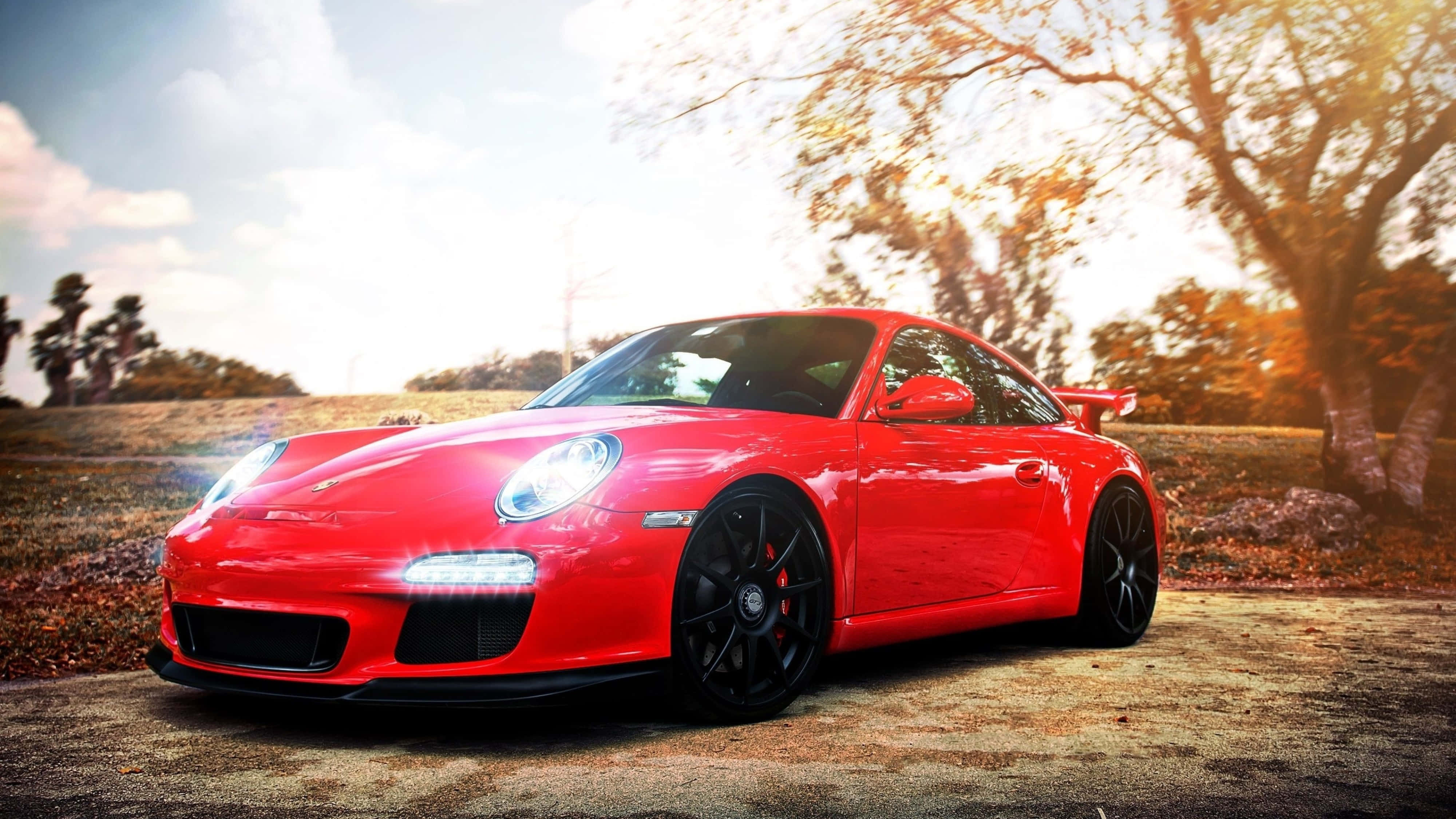 桌布 壁紙 — 一輛鮮紅色的保時捷911 GT3 RS在金色夕陽下閃耀，停泊在秋天樹木旁的泥路上。