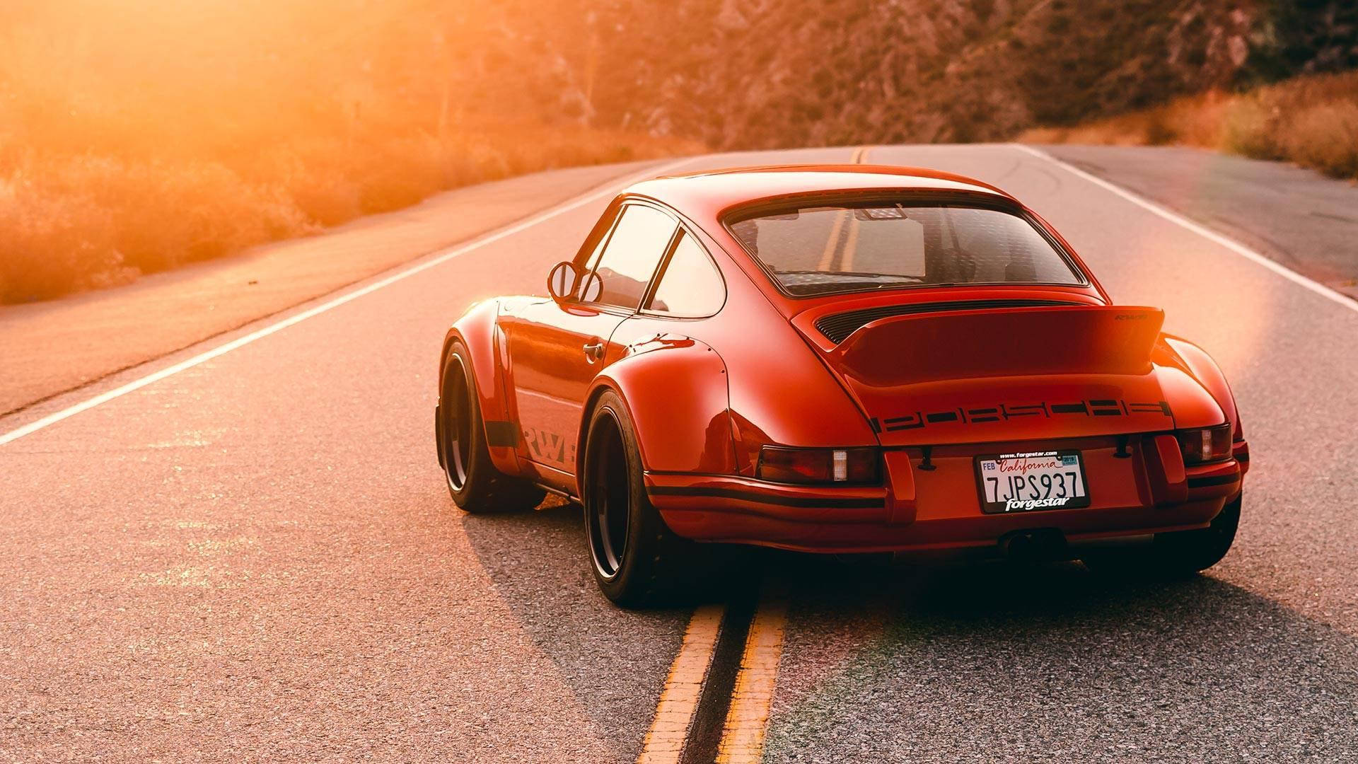 Porsche 911 桌布 壁紙 — 一輛鮮紅色的保時捷911 Turbo在蜿蜒的道路上行駛，沐浴在金色的日落光芒中。