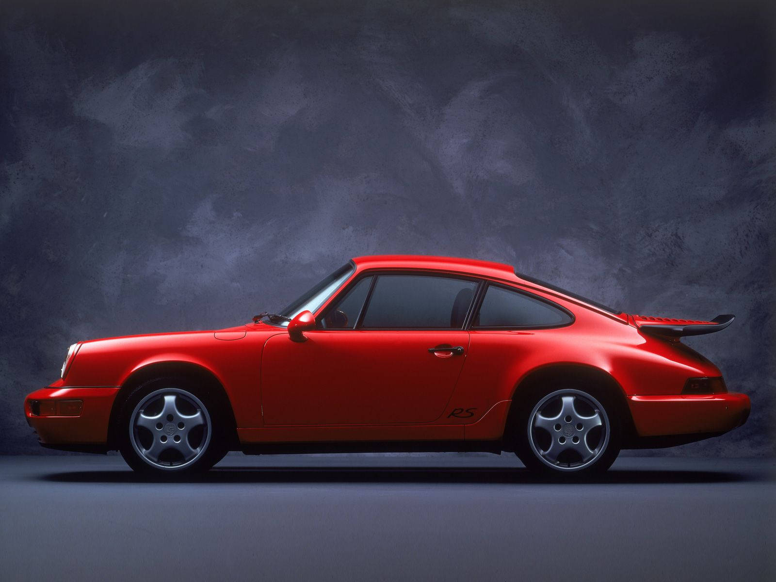 Porsche 911 桌布 壁紙 — 一輛鮮紅色的保時捷911 Turbo S在帶有紋理的深灰色工作室背景前，以戲劇性的燈光呈現側面輪廓。