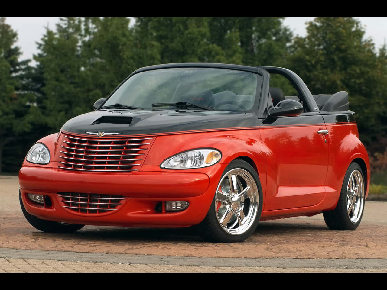 Chrysler Pt Cruiser 桌布 壁紙 — 一輛鮮紅色的克萊斯勒 PT Cruiser 敞篷車，黑色車頂，停放在磚砌車道上，周圍綠樹環繞。