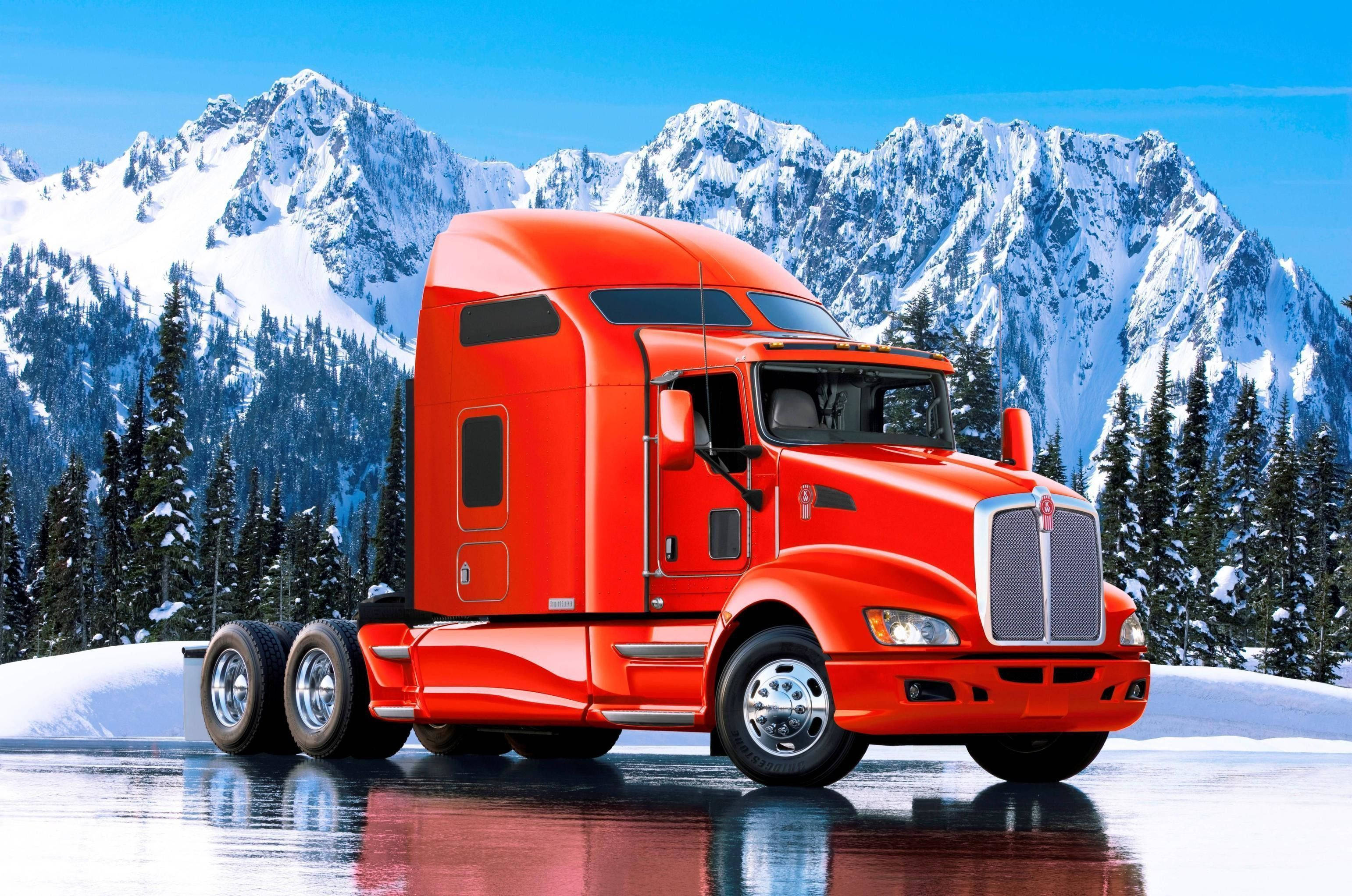 Kenworth 桌布 壁紙 — 一輛鮮紅色的半掛卡車停在冰雪地形上，背景有白雪覆蓋的山脈和常綠樹，天空清澈湛藍。