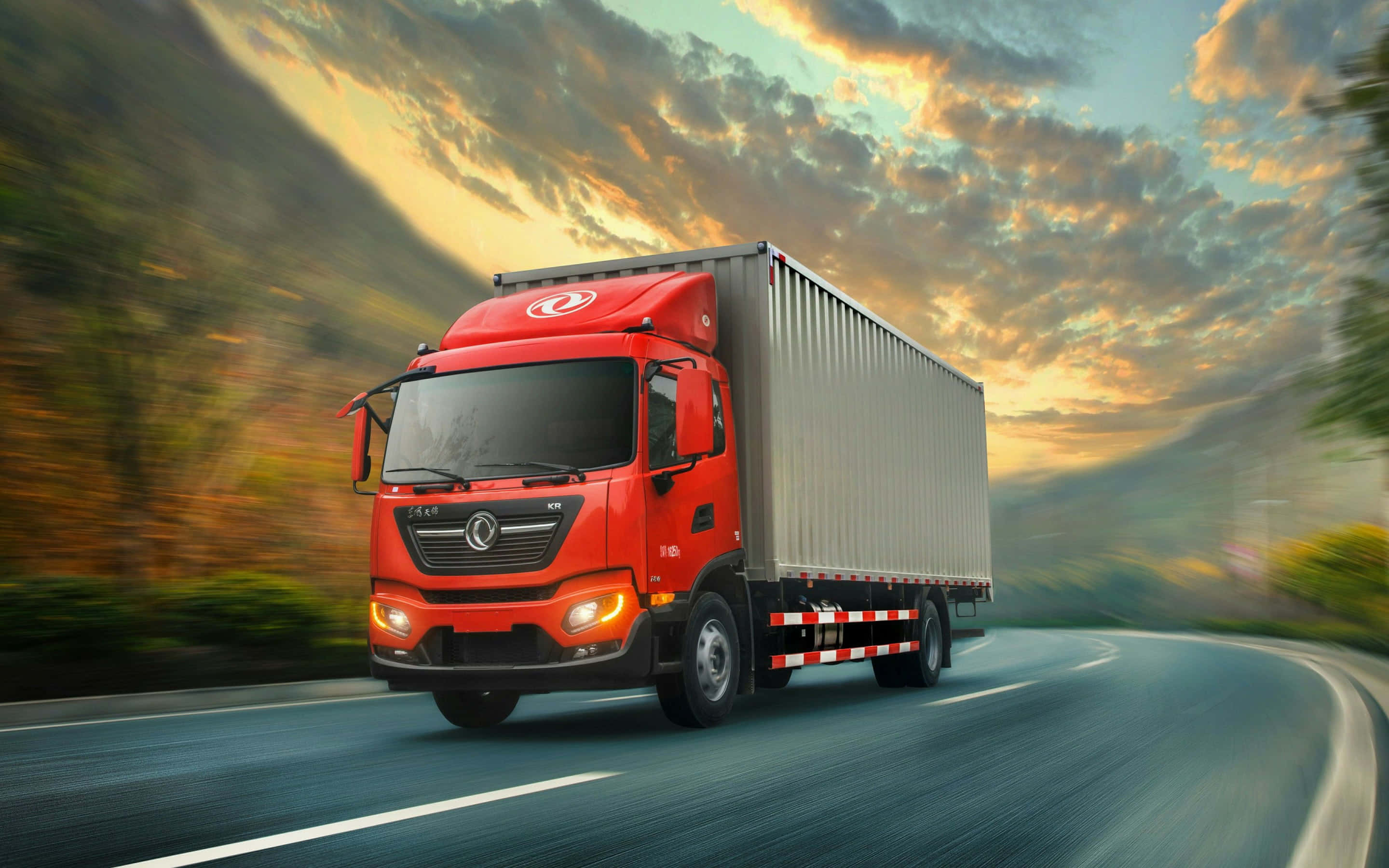 Dongfeng 桌布 壁紙 — 一輛鮮紅色的半掛卡車在戲劇性的日落天空下，沿著蜿蜒的道路疾馳，天空中有金色的雲彩。
