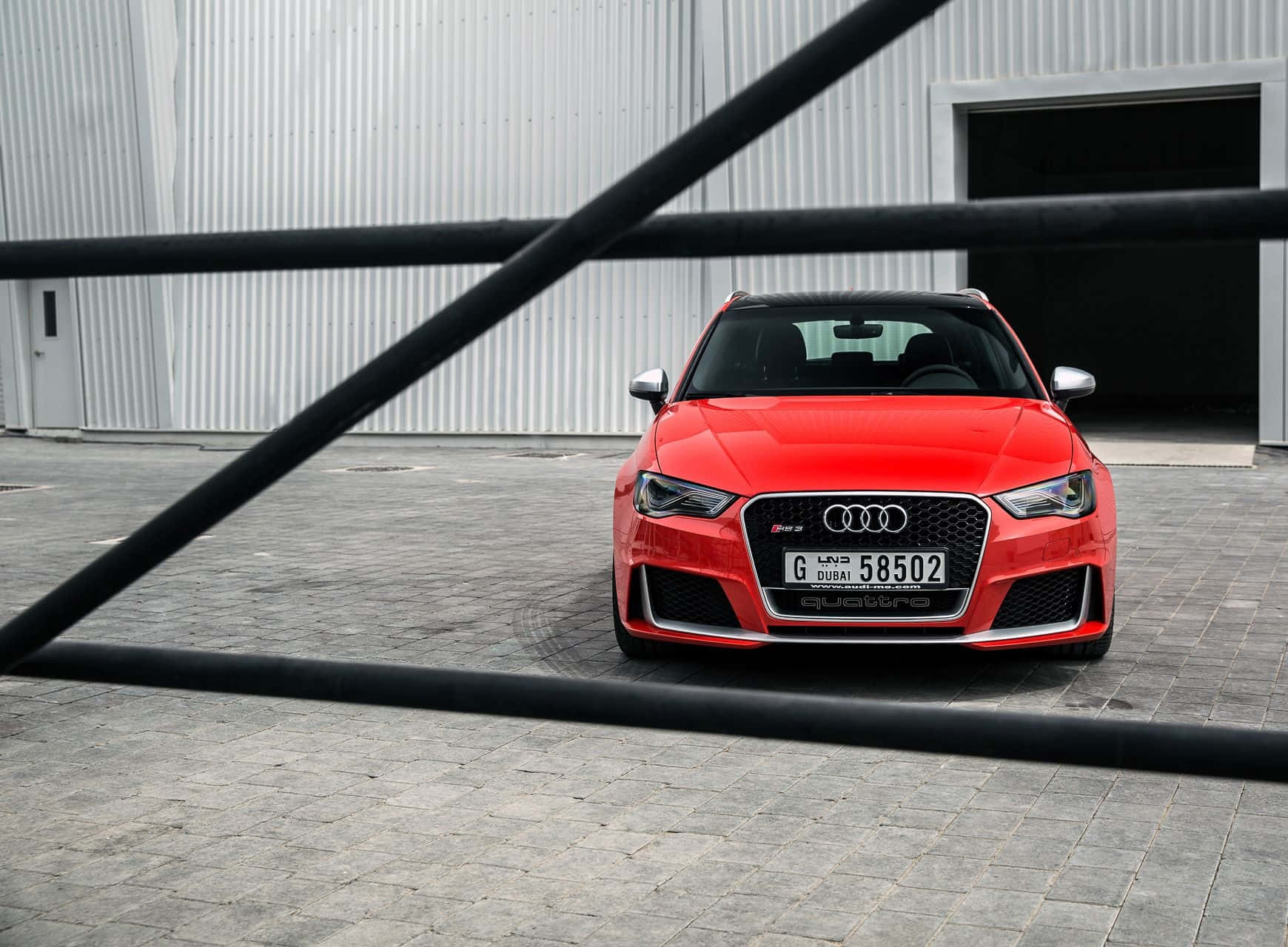 Audi Rs3 桌布 壁紙 — 一輛鮮紅色的奧迪RS3跑車停在灰色磚砌庭院中，由黑色金屬欄杆框住，後面有一座波紋金屬建築。
