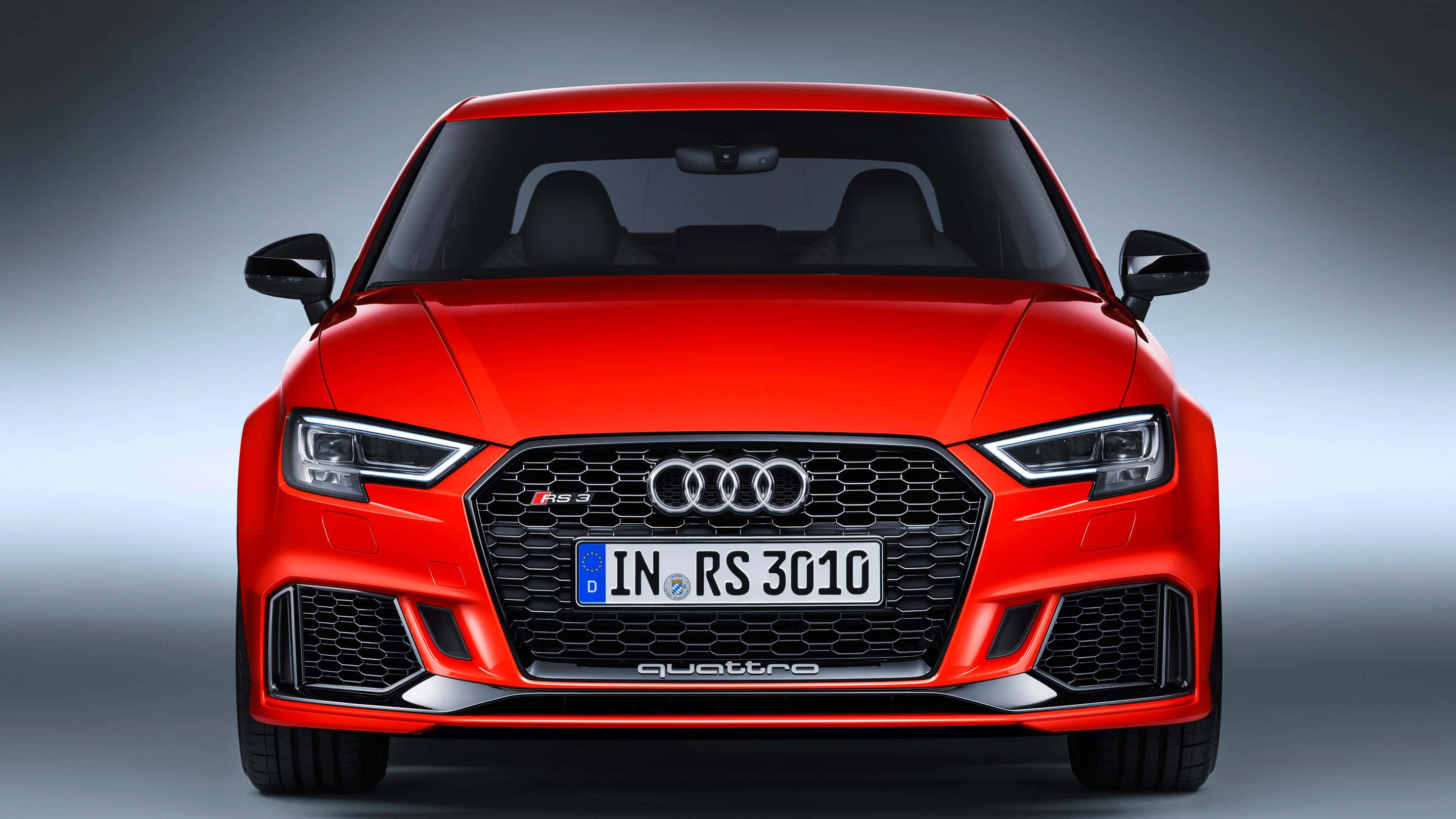 Audi Rs3 桌布 壁紙 — 一輛鮮紅色的奧迪RS3跑車正面朝前，具有侵略性造型和銳利的LED頭燈，背景為漸變工作室背景。