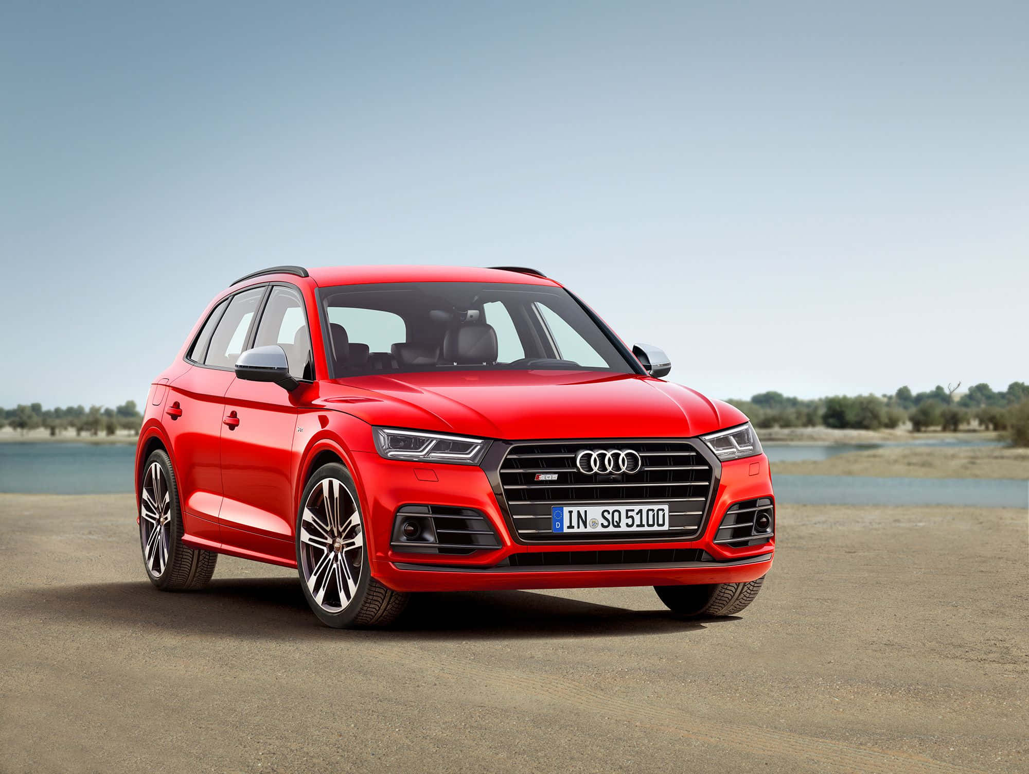 Audi Sq5 桌布 壁紙 — 一輛鮮紅色的奧迪SQ5 SUV停泊在碎石岸邊，旁邊是平靜的水面，上方是清澈的藍天。
