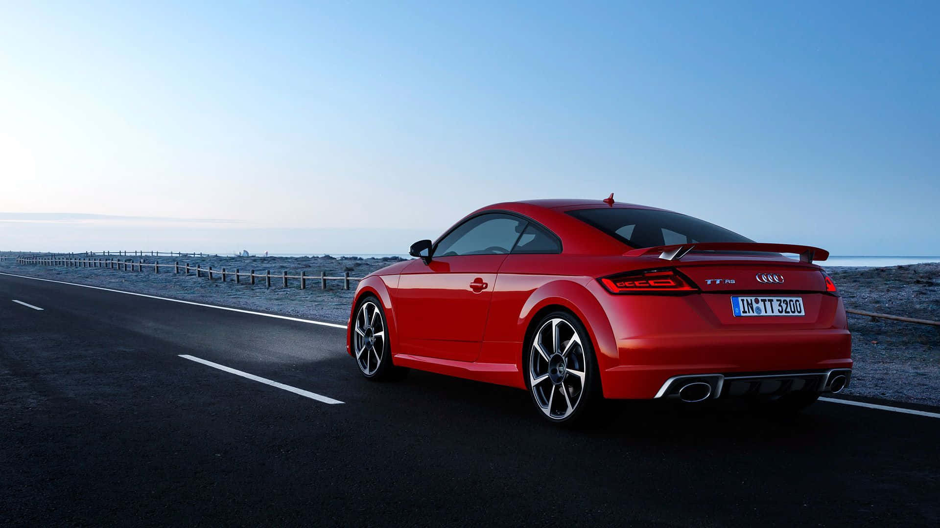 Audi Tt 桌布 壁紙 — 一輛鮮紅色的奧迪TT RS雙門跑車停泊在黎明時分的沿海道路上，天空湛藍，遠方海平線清晰可見。