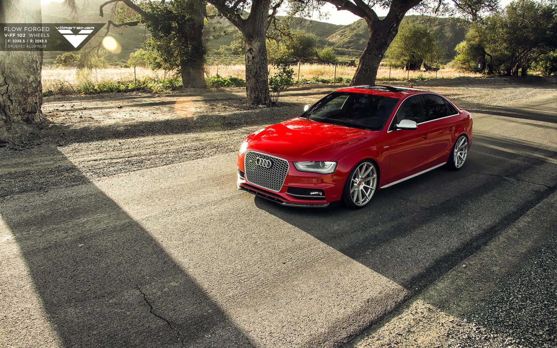 Audi S4 桌布 壁紙 — 一輛鮮紅色的奧迪跑車停放在陽光明媚的碎石路上，大樹下，背景是連綿起伏的山丘。