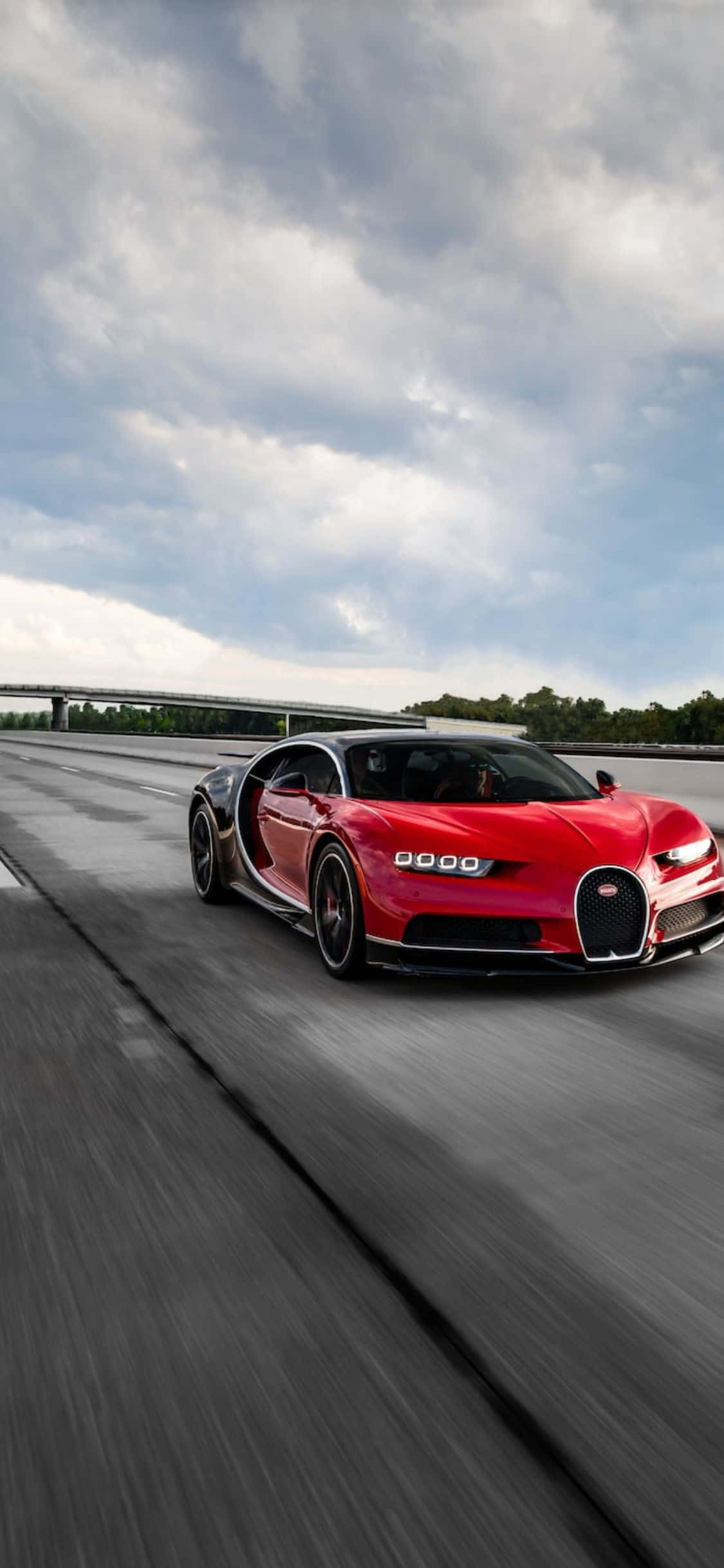 iPhone Xs Bugatti 桌布 壁紙 — 一輛鮮紅色的布加迪Chiron在潮濕的高速公路上疾馳，天空多雲，動態模糊強調了速度。