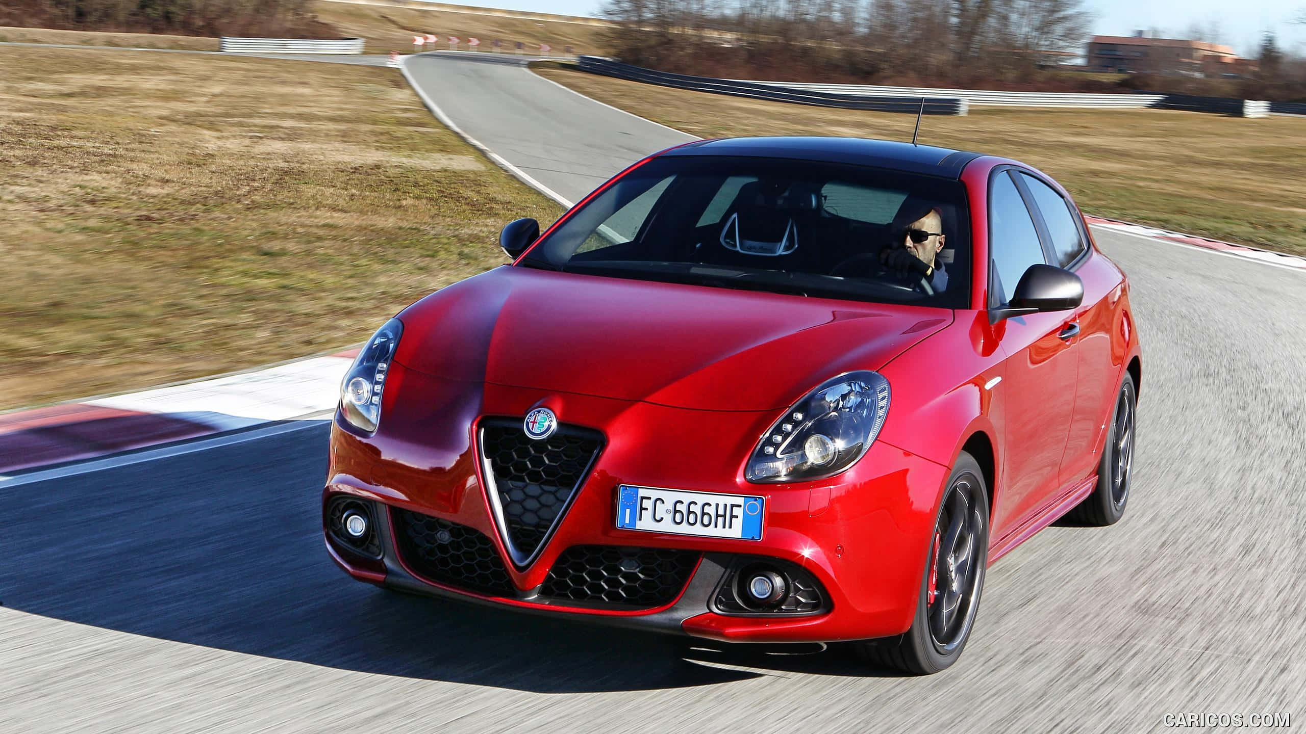 Alfa Romeo Giulietta 桌布 壁紙 — 一輛鮮紅色的愛快羅密歐 Giulietta 在晴朗日光下沿著彎曲的賽道飛馳，動態模糊效果強調了速度。