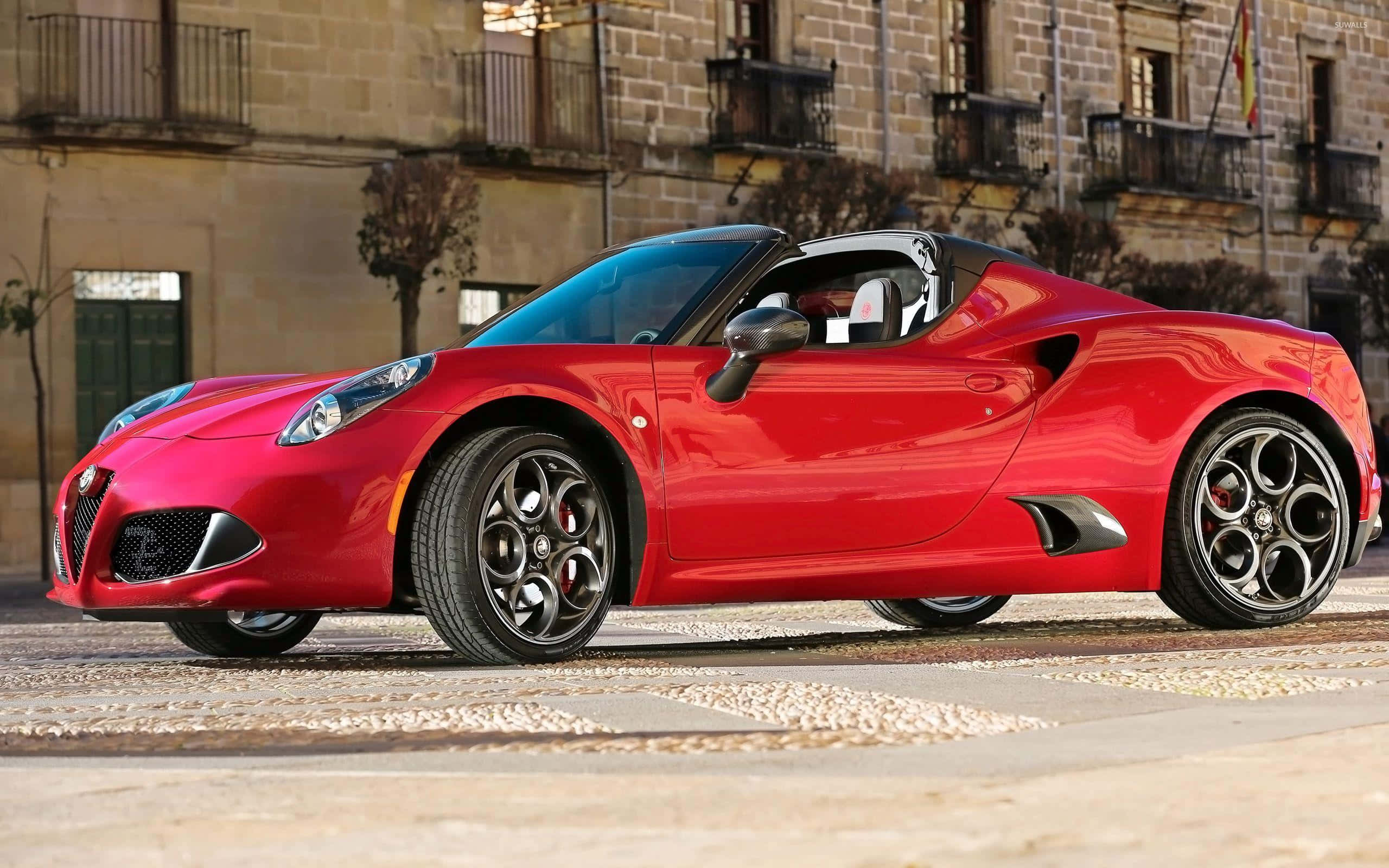 Alfa Romeo 4c 桌布 壁紙 — 一輛鮮紅色的愛快羅密歐4C Spider停放在陽光普照的鵝卵石街道上，背景是歷史悠久的石造建築。