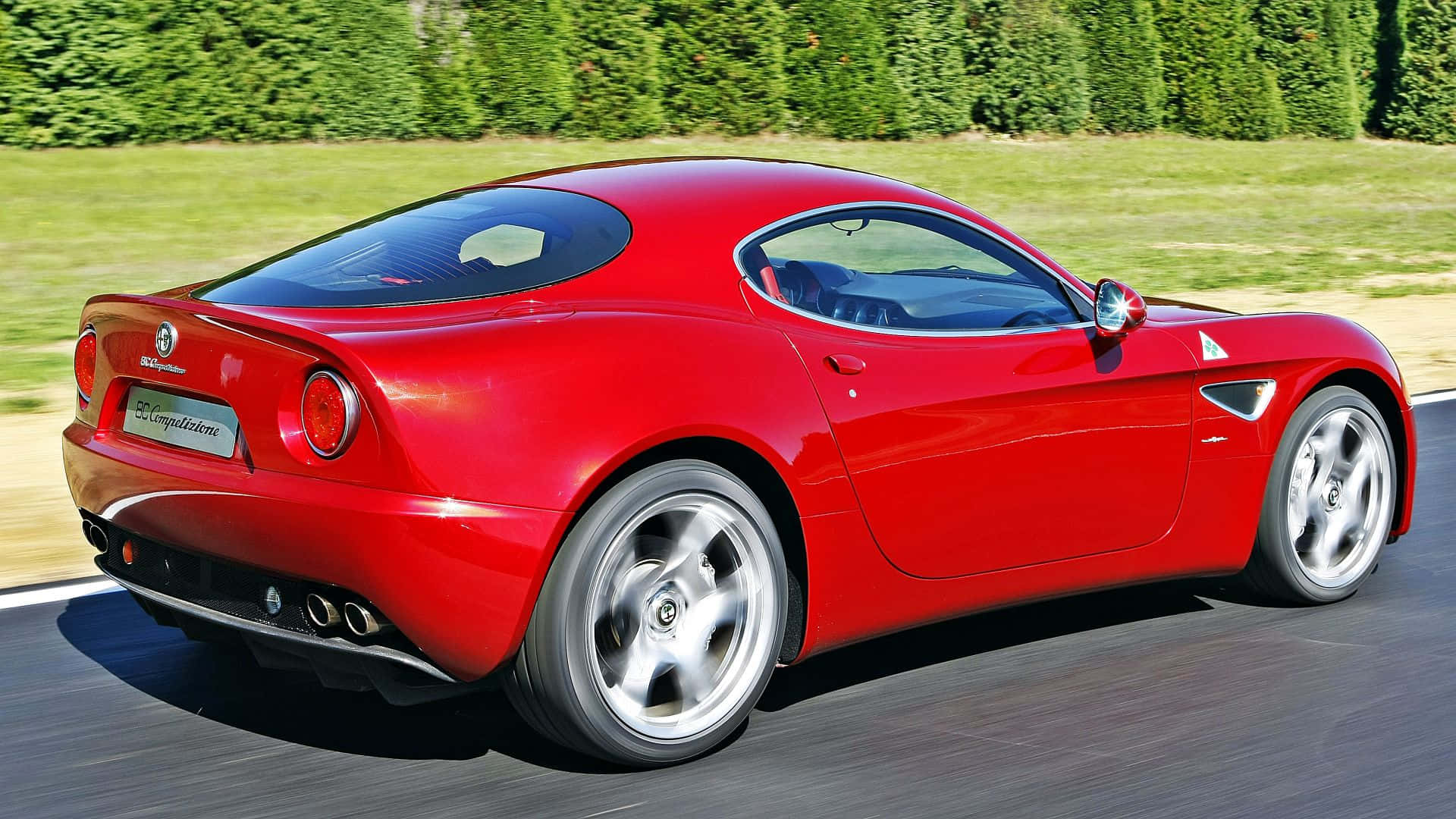 Alfa Romeo 8c Competizione 桌布 壁紙 — 一輛鮮紅色的愛快羅密歐8C Competizione跑車在陽光明媚的道路上行駛，背景是茂密的綠色樹籬。