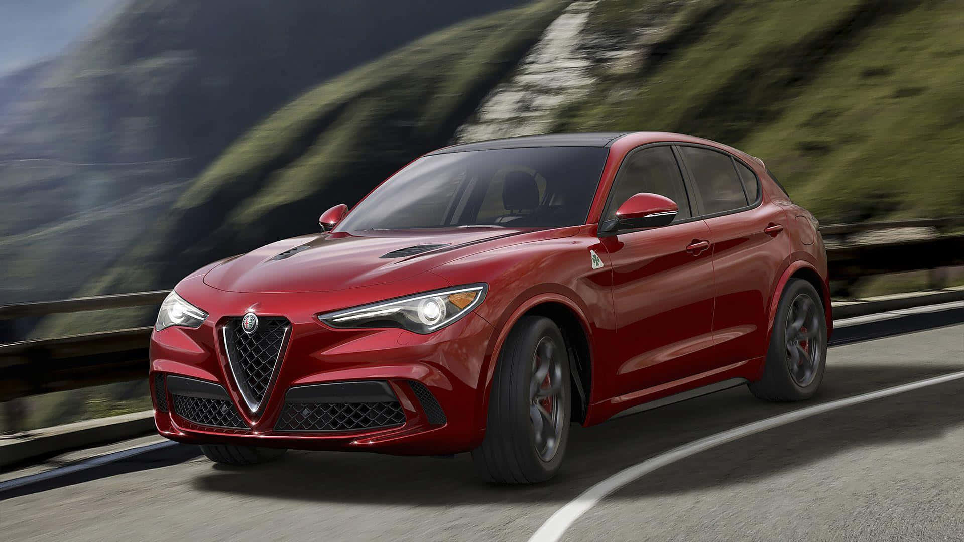 Alfa Romeo Stelvio 桌布 壁紙 — 一輛鮮紅色的愛快羅密歐Stelvio SUV沿著蜿蜒的山路飛馳，背景中鬱鬱蔥蔥的綠色山坡模糊不清。