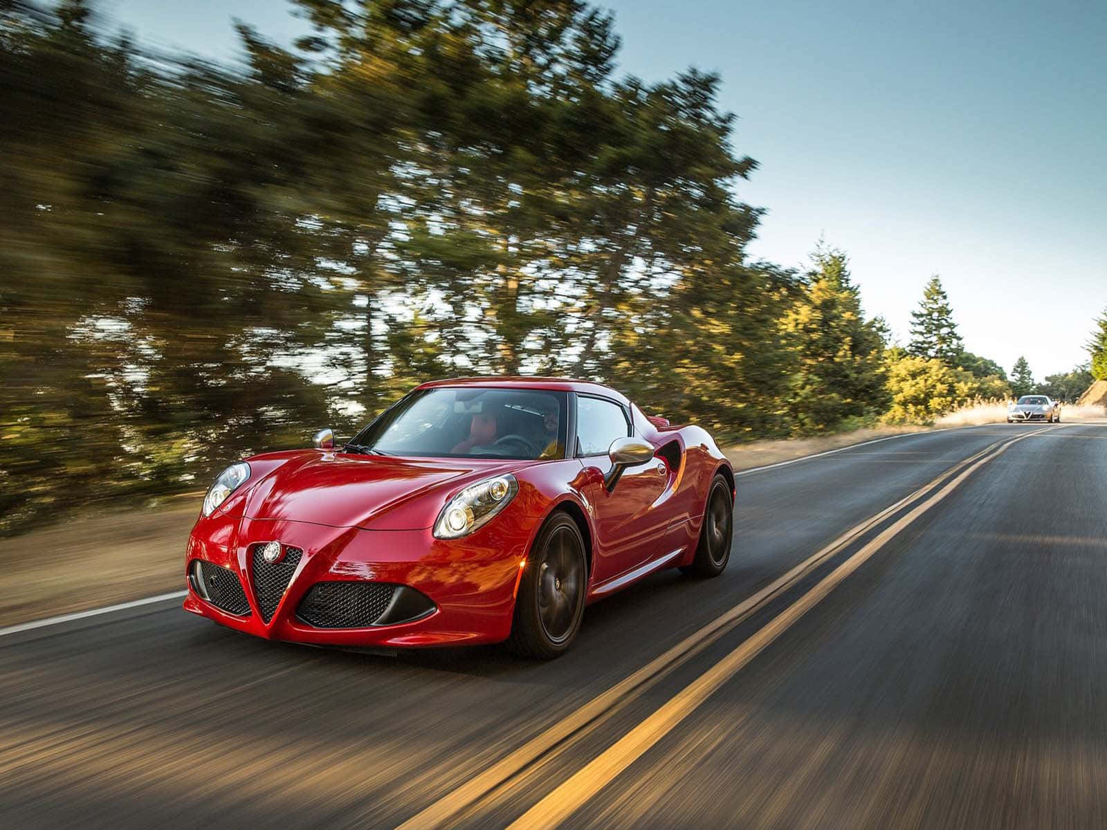 Alfa Romeo 4c 桌布 壁紙 — 一輛鮮紅色的愛快羅密歐跑車在蜿蜒的森林道路上疾馳，動態模糊效果強調了其速度。