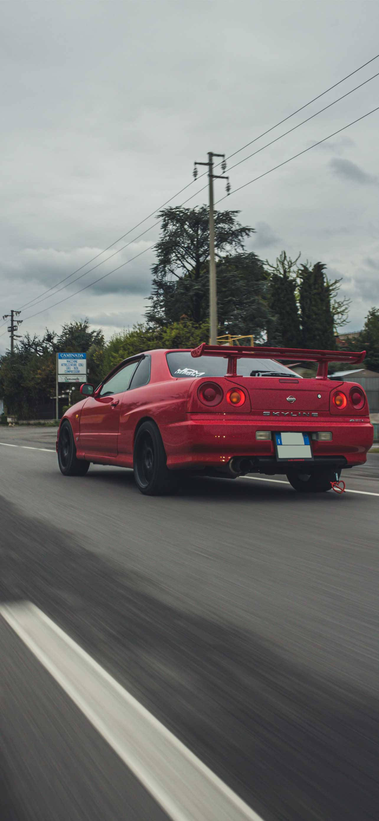 Best Car 桌布 壁紙 — 一輛鮮紅色的日產Skyline GT-R在陰天下行駛在濕滑的道路上，帶有動態模糊效果。
