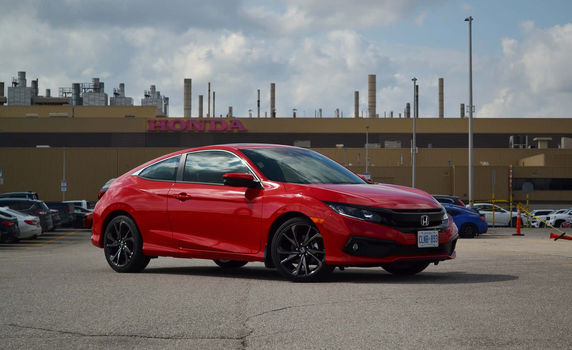 Honda Civic 桌布 壁紙 — 一輛鮮紅色的本田思域轎跑車停在停車場，背景是工廠和多雲的天空。