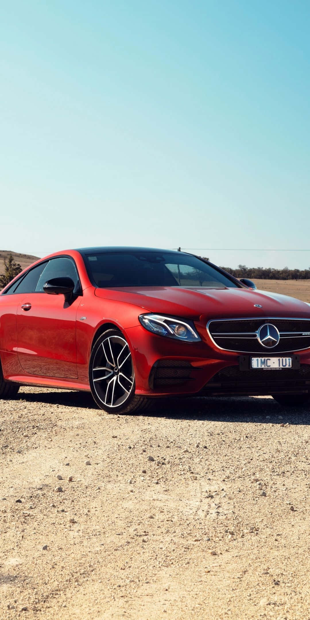 Red Car 桌布 壁紙 — 一輛鮮紅色的梅賽德斯-奔馳E-Class雙門轎跑車停放在陽光普照的碎石地上，背景是清澈的藍天。