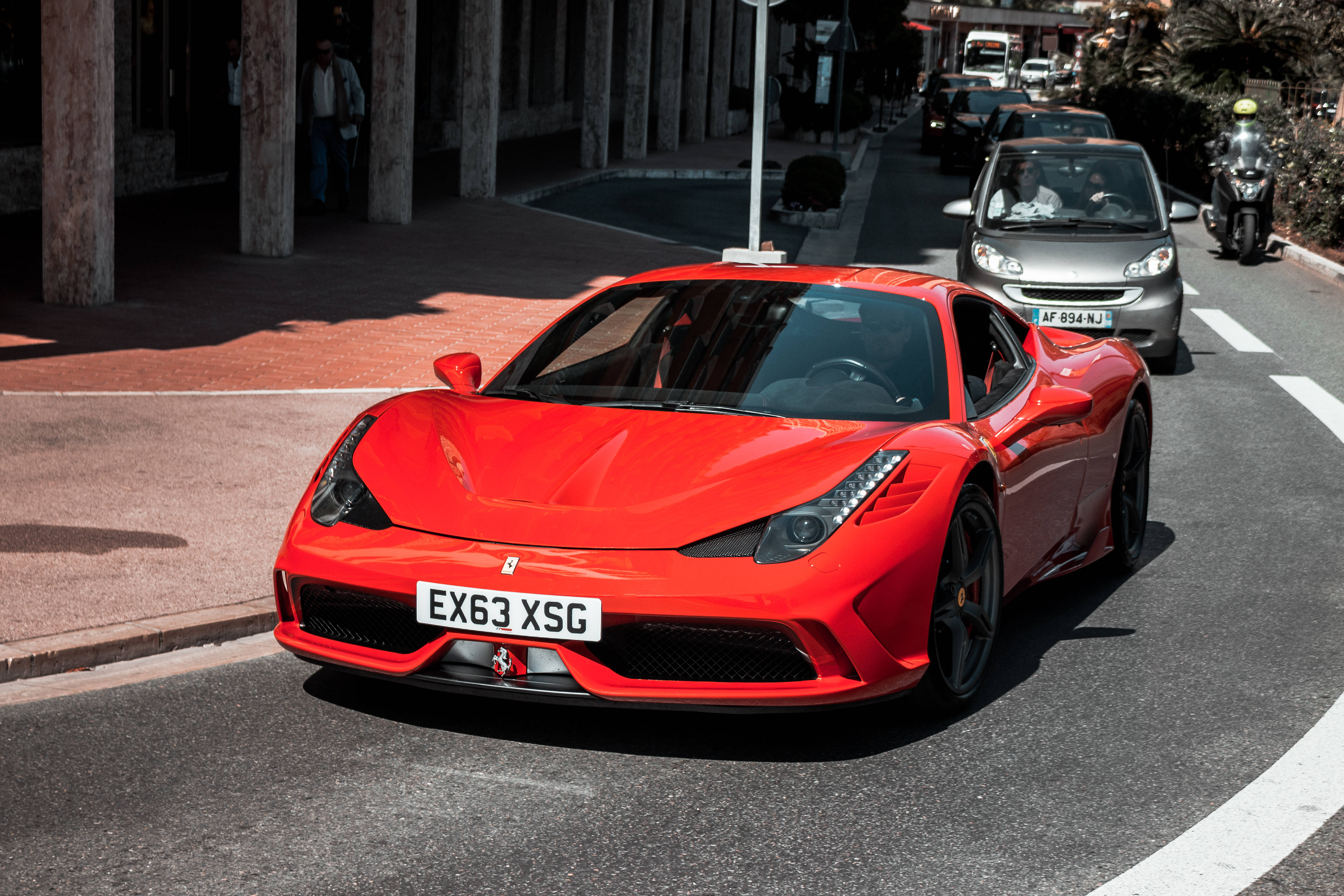 Monaco 桌布 壁紙 — 一輛鮮紅色的法拉利 488 GTB 在陽光明媚的城市街道上行駛，背景有行人和車輛。