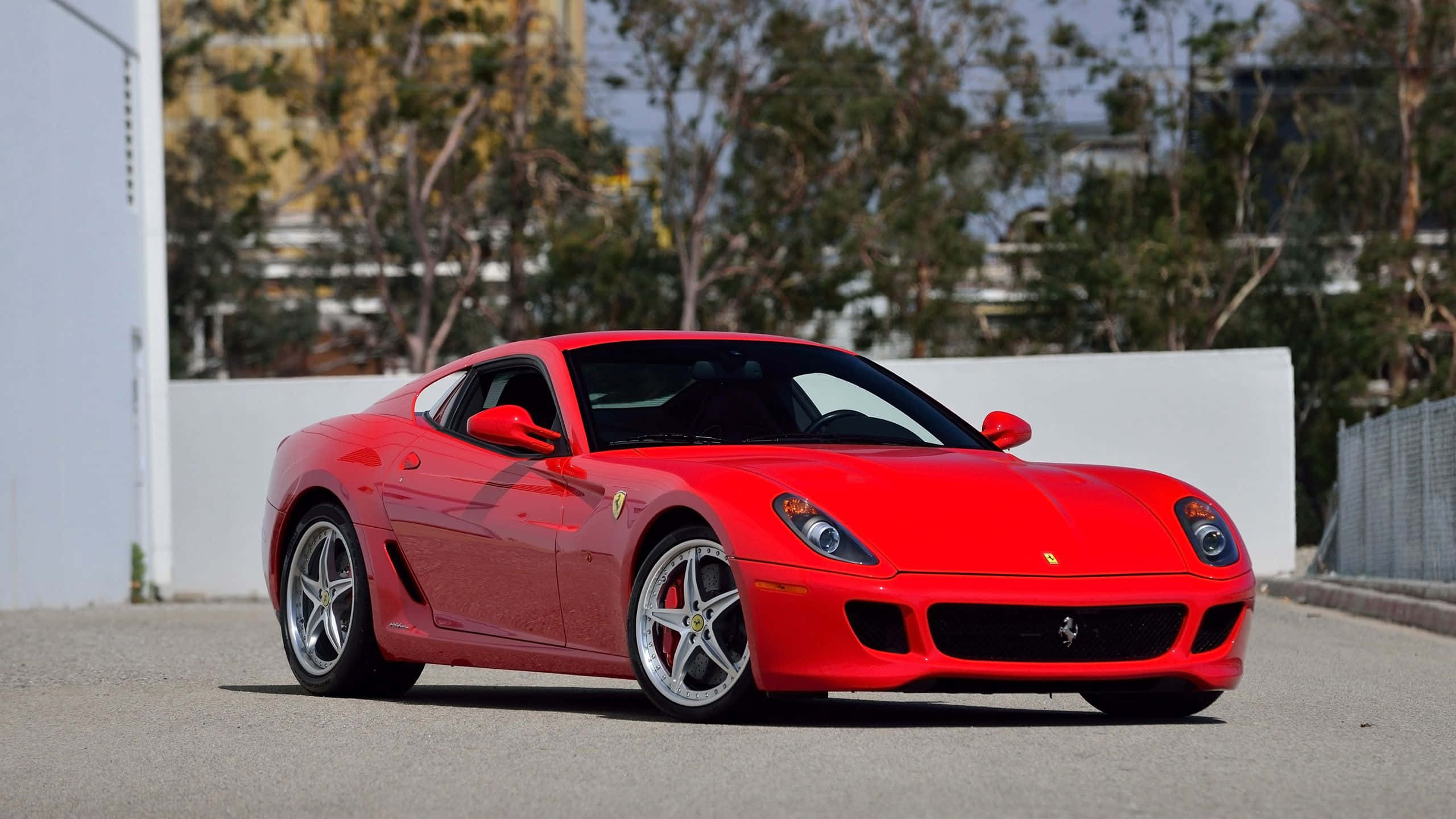 Ferrari 599 Gtb Fiorano 桌布 壁紙 — 一輛鮮紅色的法拉利 599 GTB Fiorano 停放在鋪砌路面上，背景有樹木和白色牆壁。