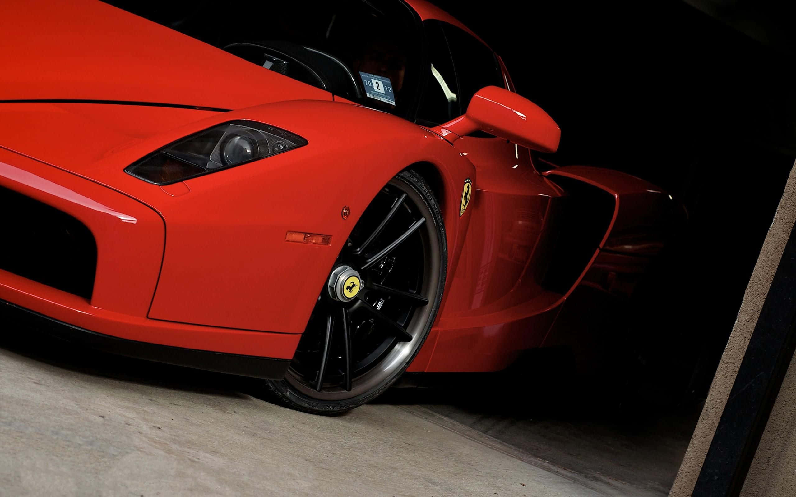 Ferrari Enzo 桌布 壁紙 — 一輛鮮紅色的法拉利 Enzo 在昏暗的車庫中，在戲劇性的燈光下閃閃發光，展現其流線型的空氣動力學設計和黑色車輪。