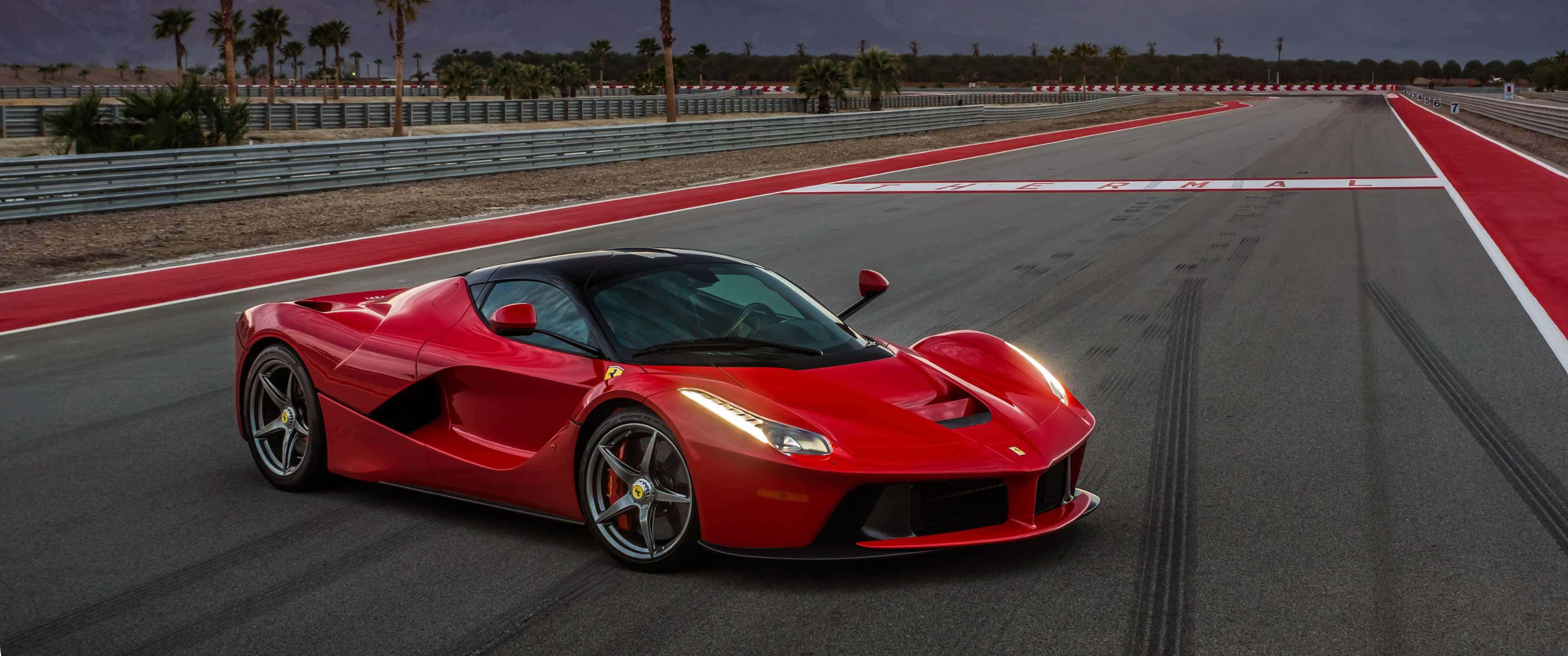汽車 桌布 壁紙 — 一輛鮮紅色的法拉利 LaFerrari 在黃昏時分沿著賽道飛馳，棕櫚樹排列在地平線上。