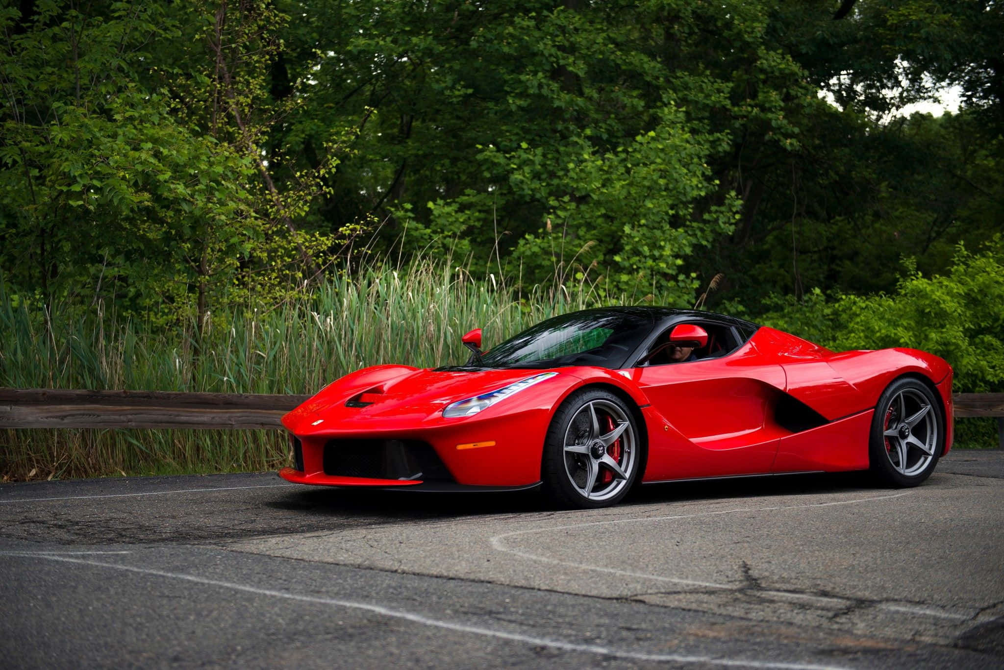 Ferrari Laferrari 桌布 壁紙 — 一輛鮮紅色的法拉利 LaFerrari 停泊在蜿蜒的道路上，周圍環繞著茂密的綠樹和高草。