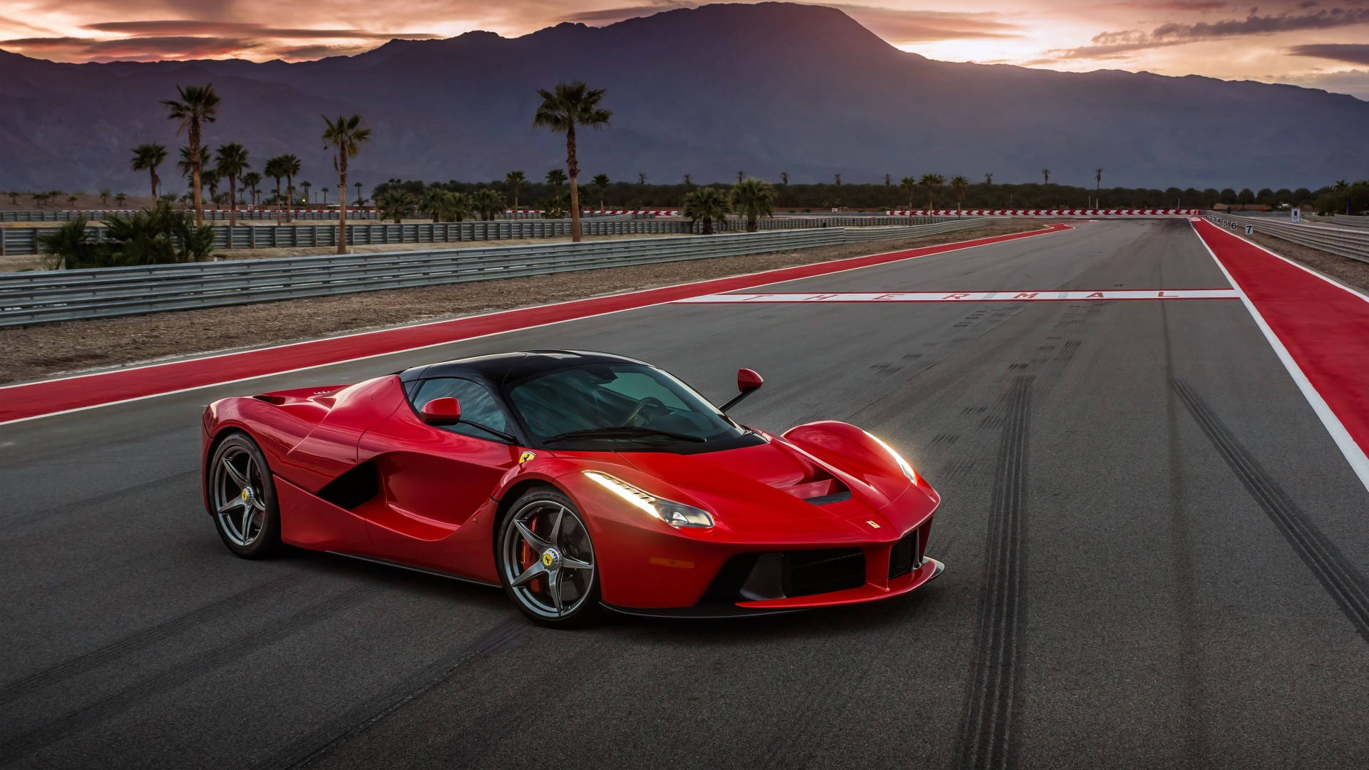 日落時分賽道上的紅色法拉利 LaFerrari，背景有山脈和棕櫚樹。 — 法拉利 GIF 壁紙