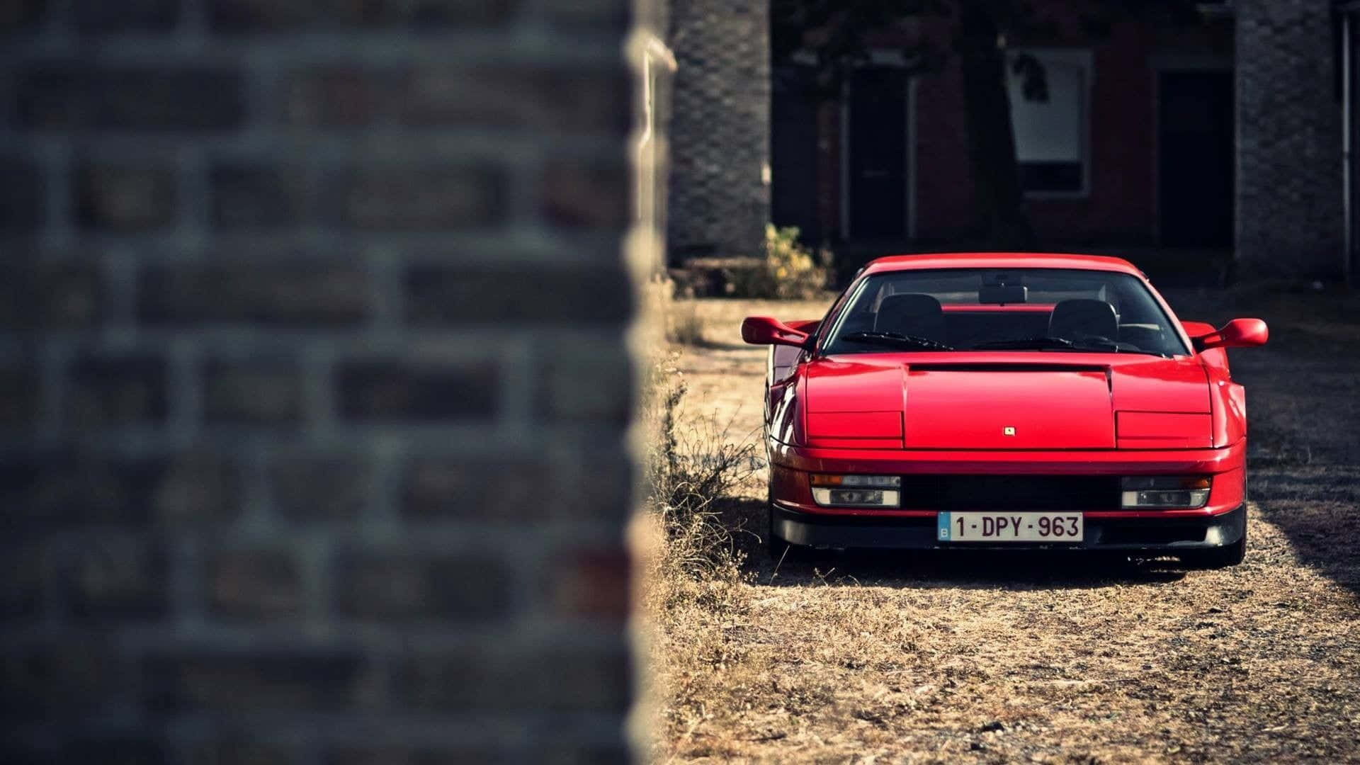 Ferrari Testarossa 桌布 壁紙 — 一輛鮮紅色的法拉利288 GTO在明亮的日光下停放在磚牆之間的乾草地上。