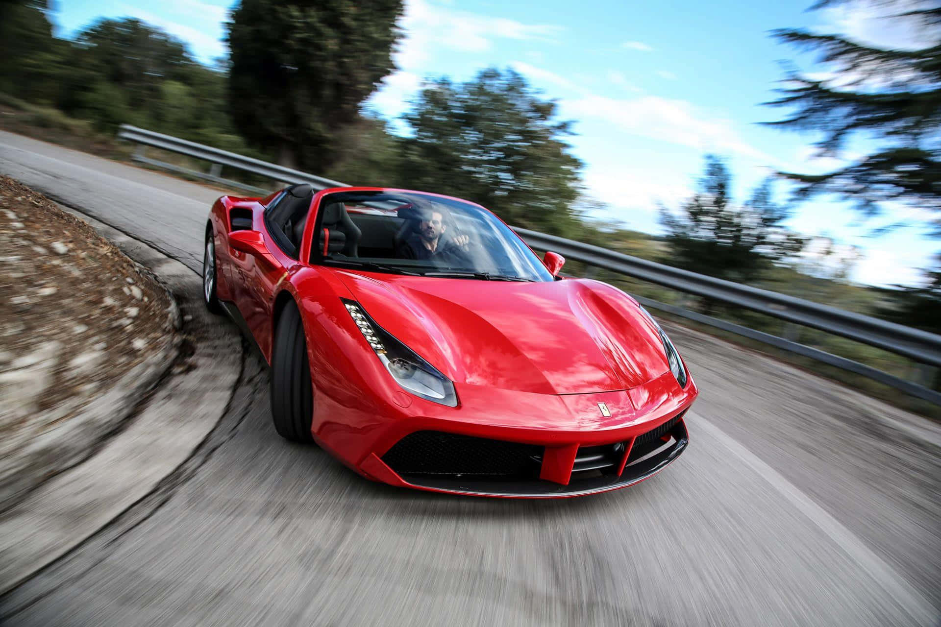 Ferrari 488 Spider 桌布 壁紙 — 一輛鮮紅色的法拉利488 Spider在蜿蜒的山路上奔馳，背景是模糊的綠樹和藍天。