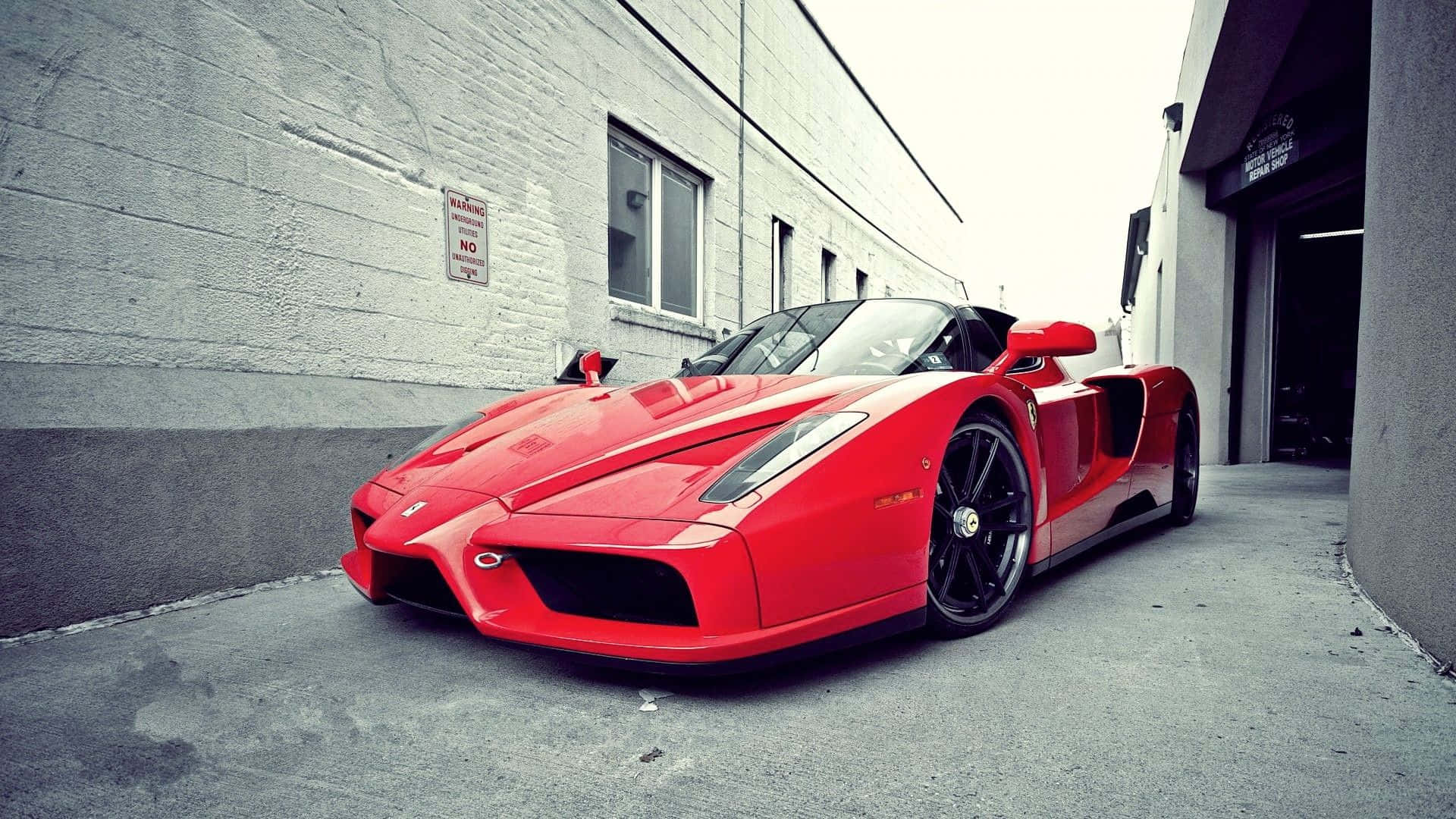 Ferrari Enzo 桌布 壁紙 — 一輛鮮紅色的法拉利Enzo停放在灰色混凝土建築之間的狹窄小巷中，天空多雲。