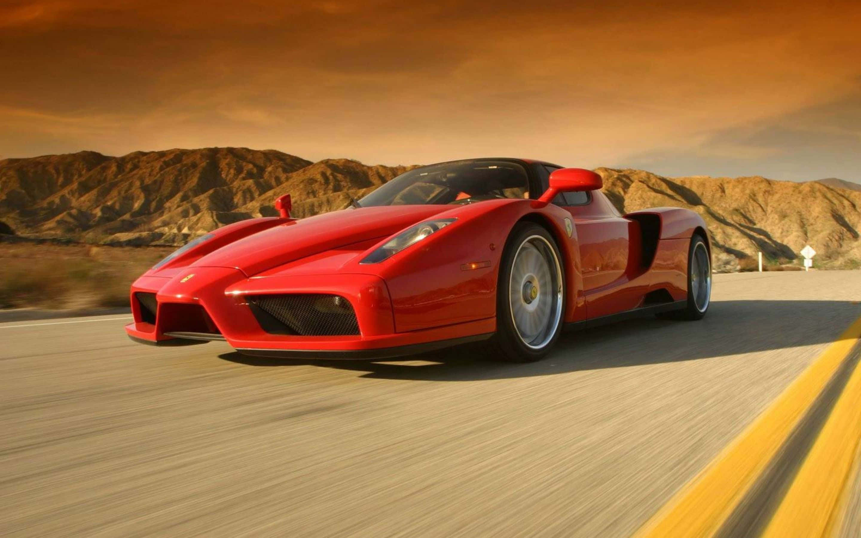 Ferrari Enzo 桌布 壁紙 — 一輛鮮紅色的法拉利Enzo在溫暖的橙色天空下，沿著崎嶇山脈的沙漠高速公路疾馳。