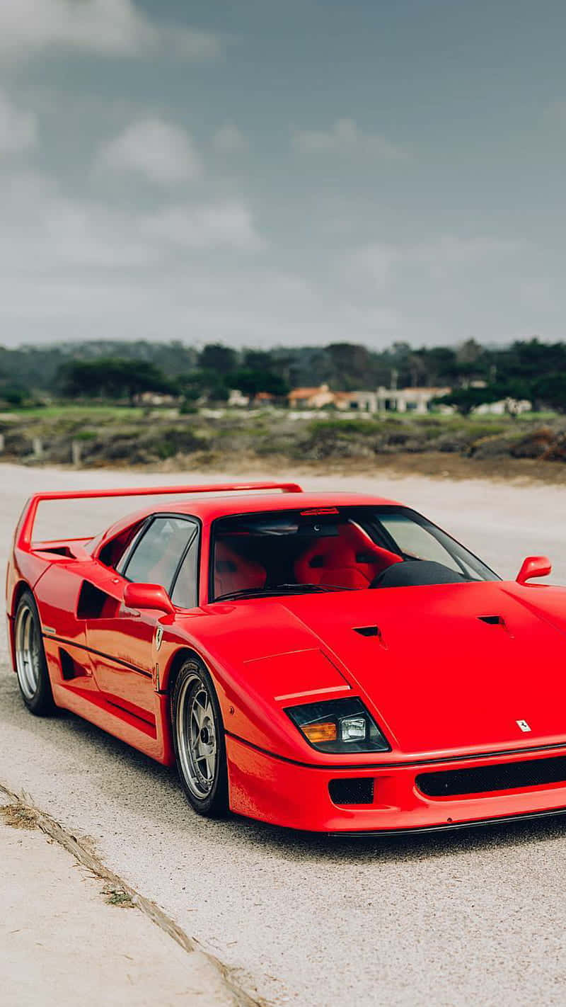 Vintage Ferrari 桌布 壁紙 — 一輛鮮紅色的法拉利F40跑車停泊在碎石路上，天空多雲，遠處有樹木和房屋。