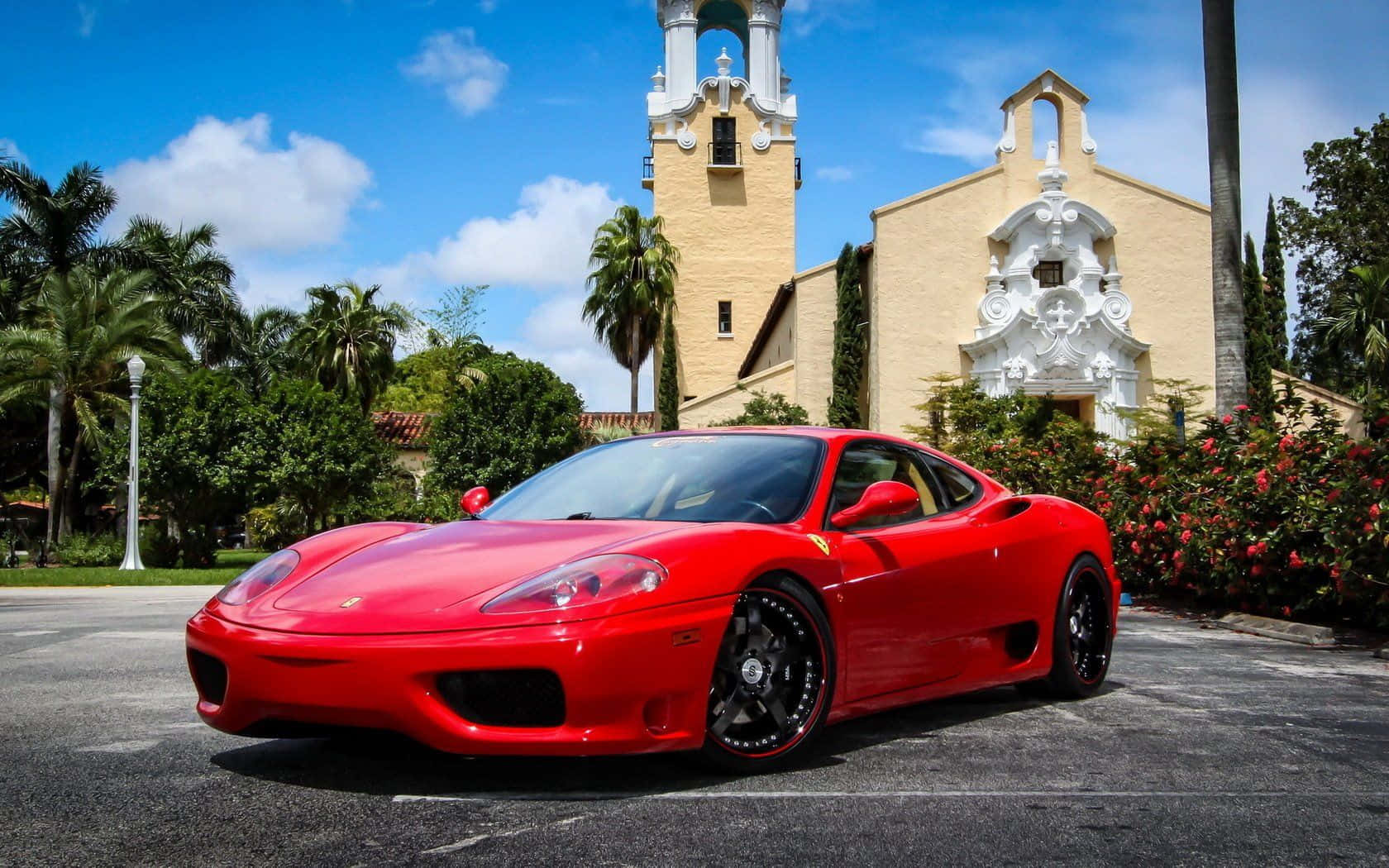Ferrari 360 Modena 桌布 壁紙 — 一輛鮮紅色的法拉利跑車停在一座西班牙風格教堂前，背景是晴朗的藍天和蓬鬆的白雲。