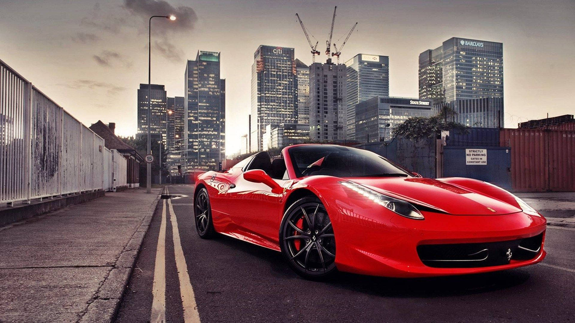 1920x1080 Ferrari 桌布 壁紙 — 一輛鮮紅色的法拉利跑車停泊在都市街道上，背景是暮色中高聳的玻璃摩天大樓和建築起重機。